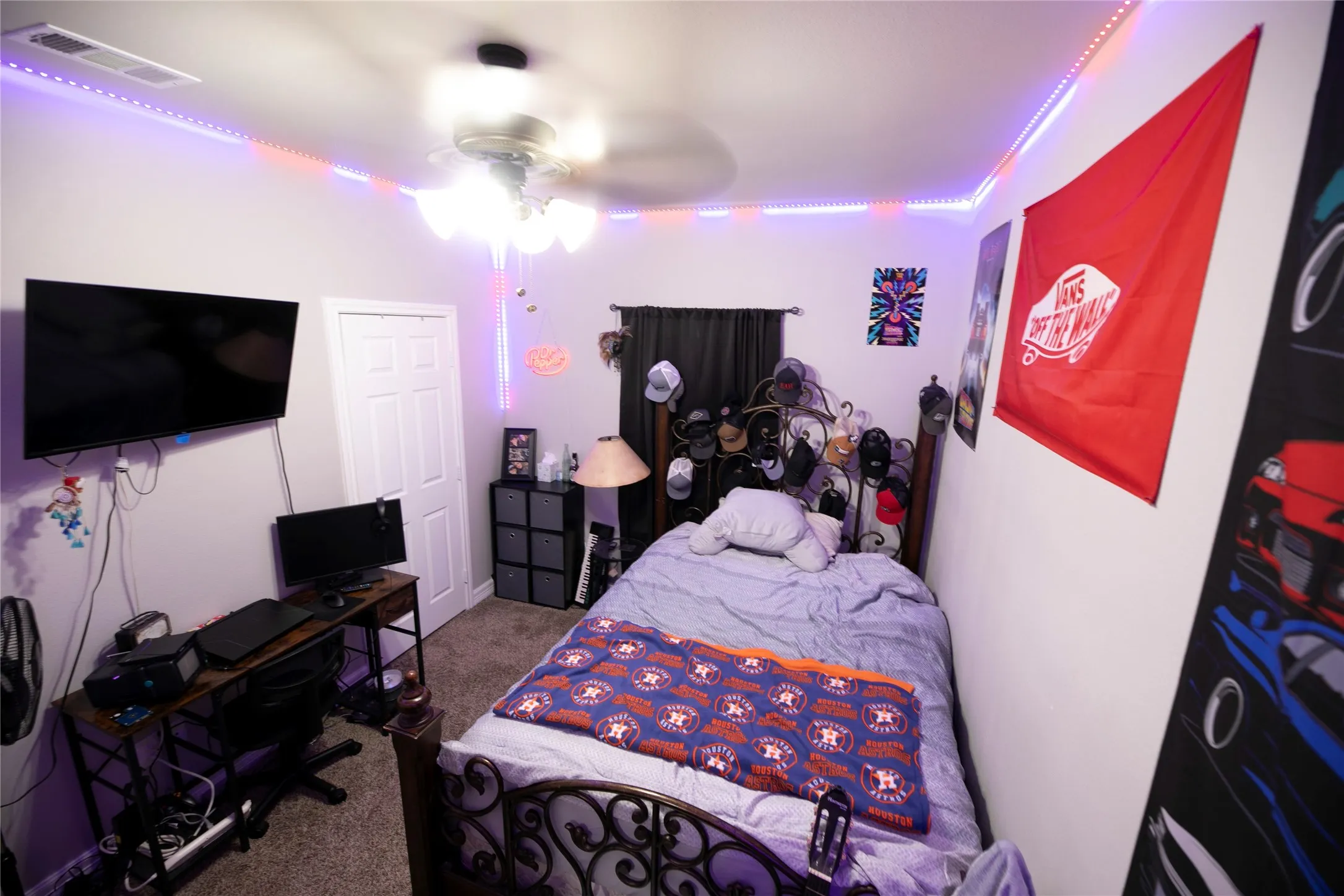 Bedroom featuring neutral wall paint, carpet flooring, a ceiling fan with integrated lighting, a wall-mounted television, and a white paneled door