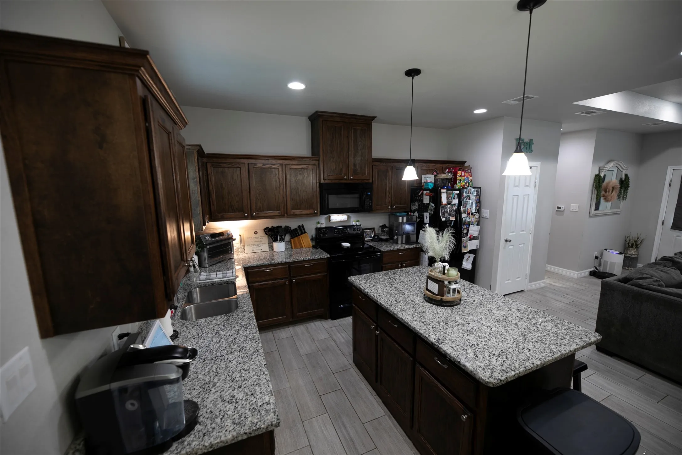 Kitchen featuring dark wood cabinetry, granite countertops, tile flooring, recessed lighting, and a kitchen island with pendant lighting