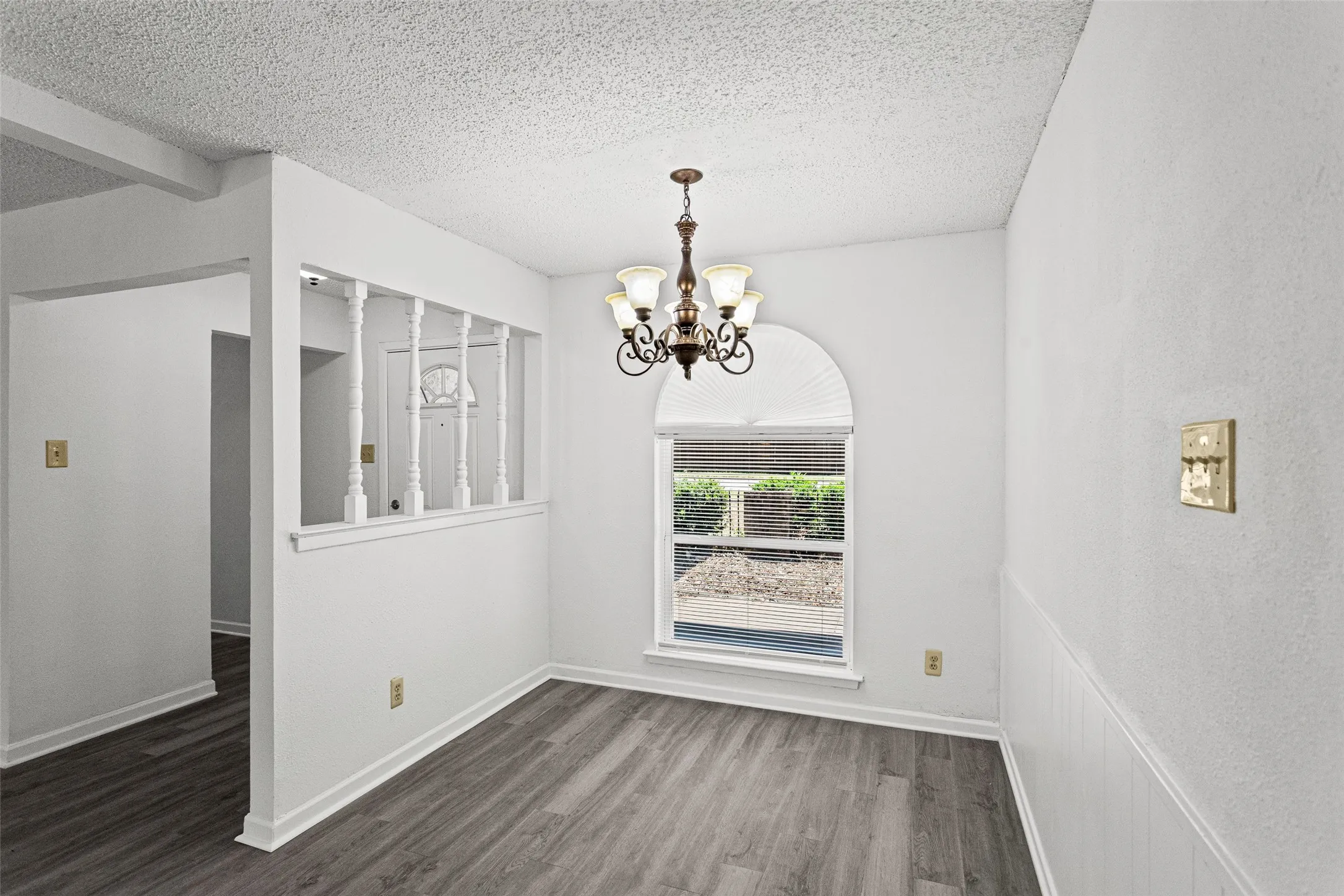 Dining area featuring a decorative chandelier, arched window with horizontal blinds, and wood-finish flooring