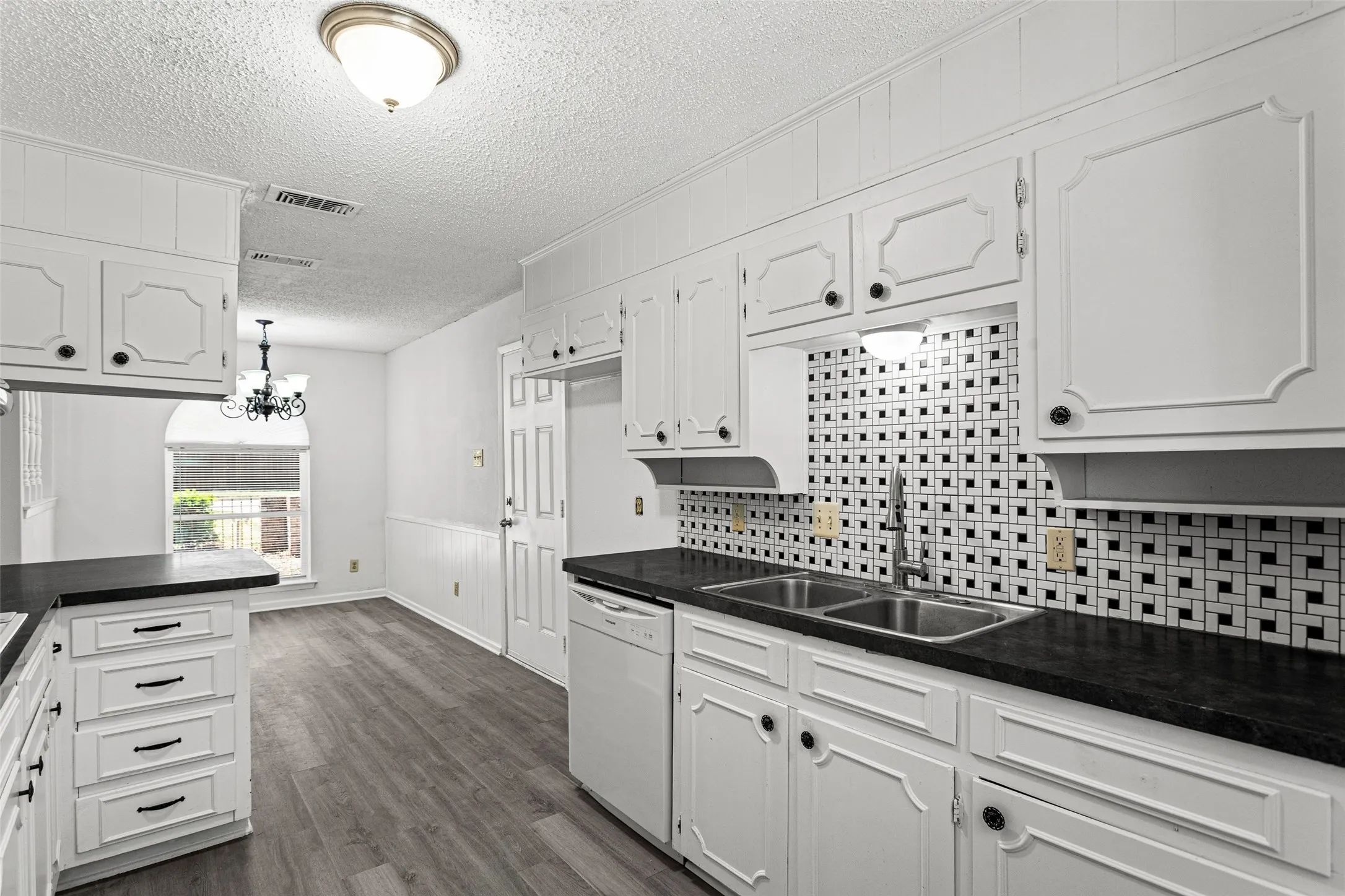 Kitchen featuring white cabinetry, dark countertops, a mosaic tile backsplash, wood-finish flooring, and a stainless steel double basin sink