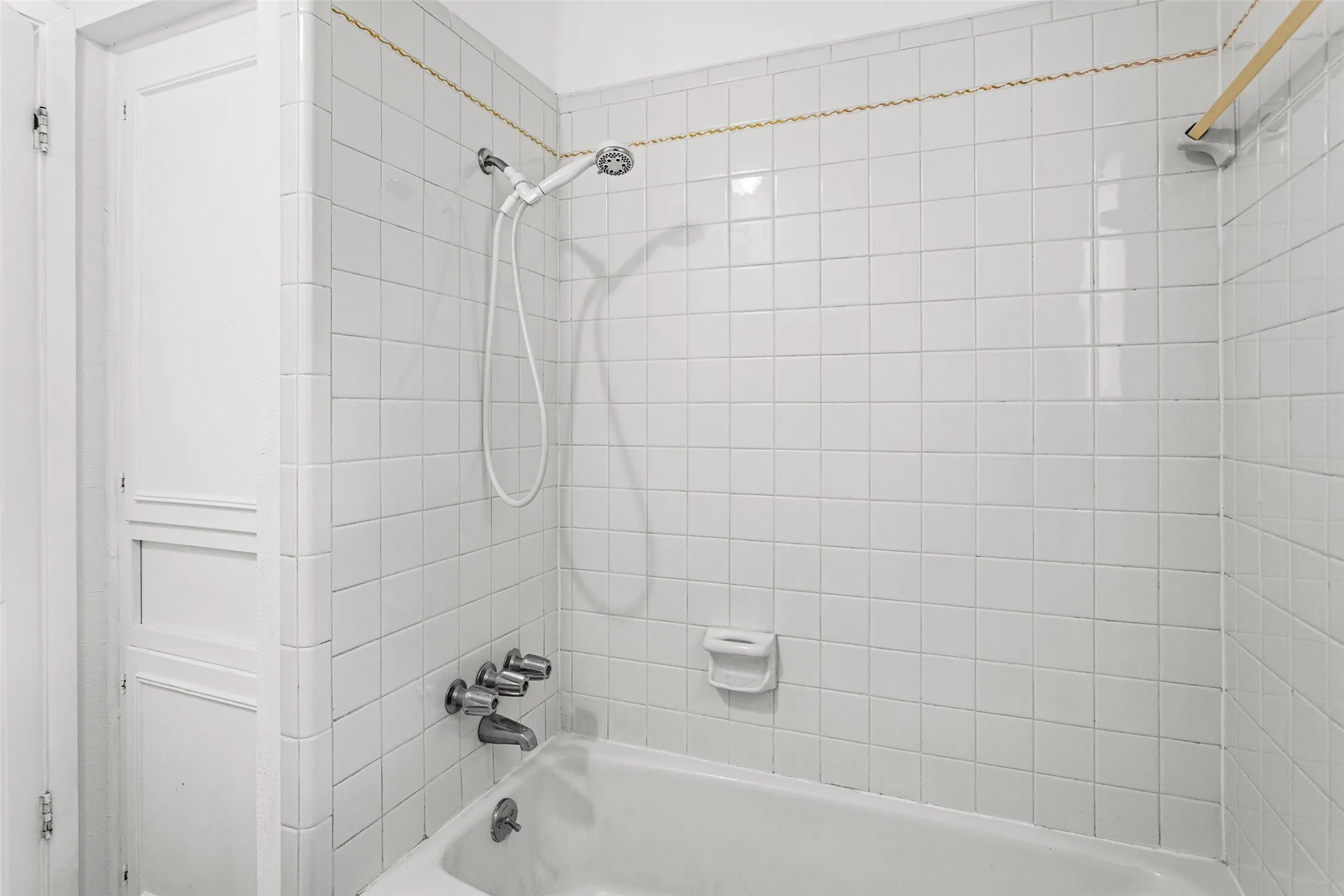 White tiled shower surround with a handheld shower head