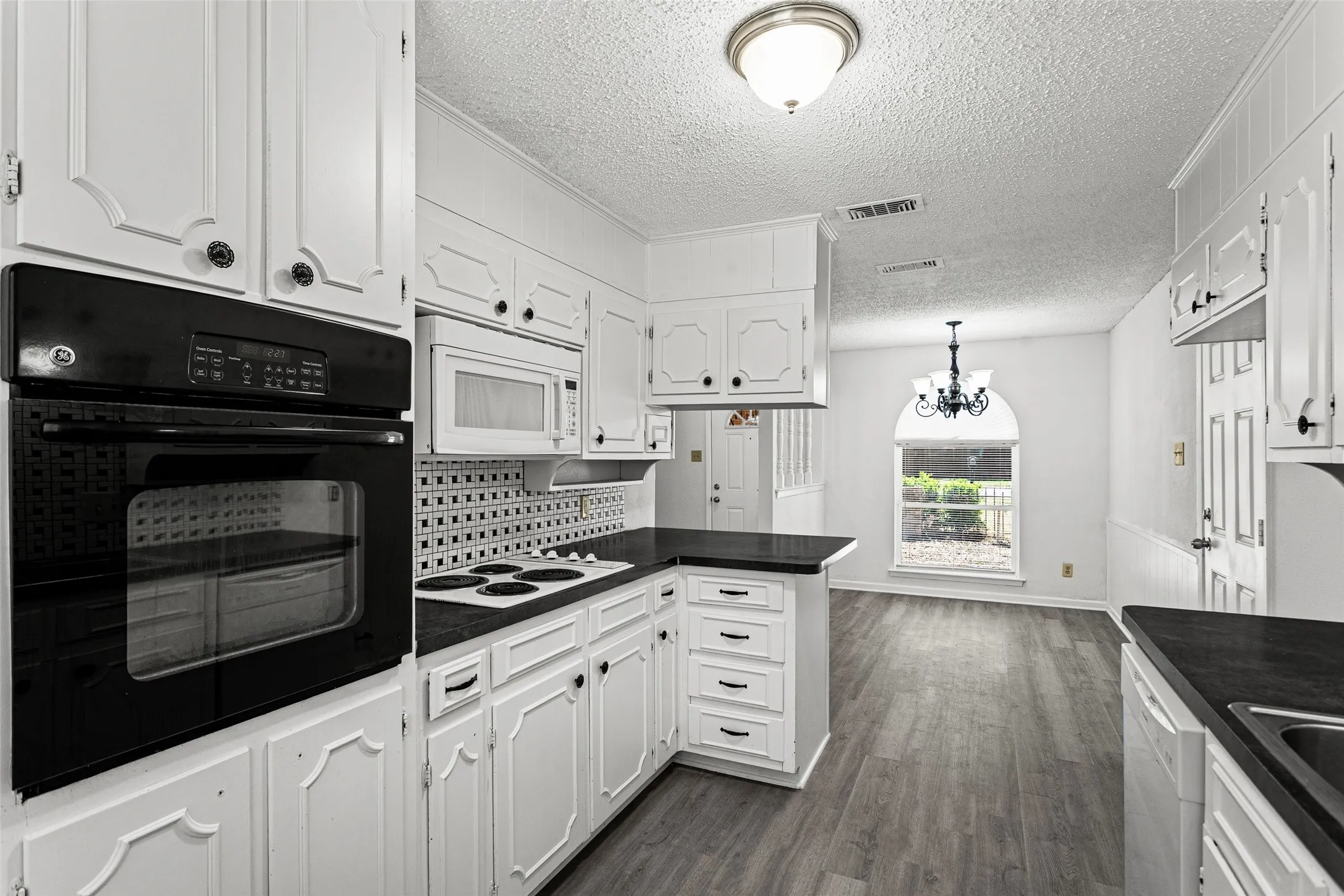 Kitchen featuring white cabinetry, dark countertops, built-in oven, and wood-finish flooring