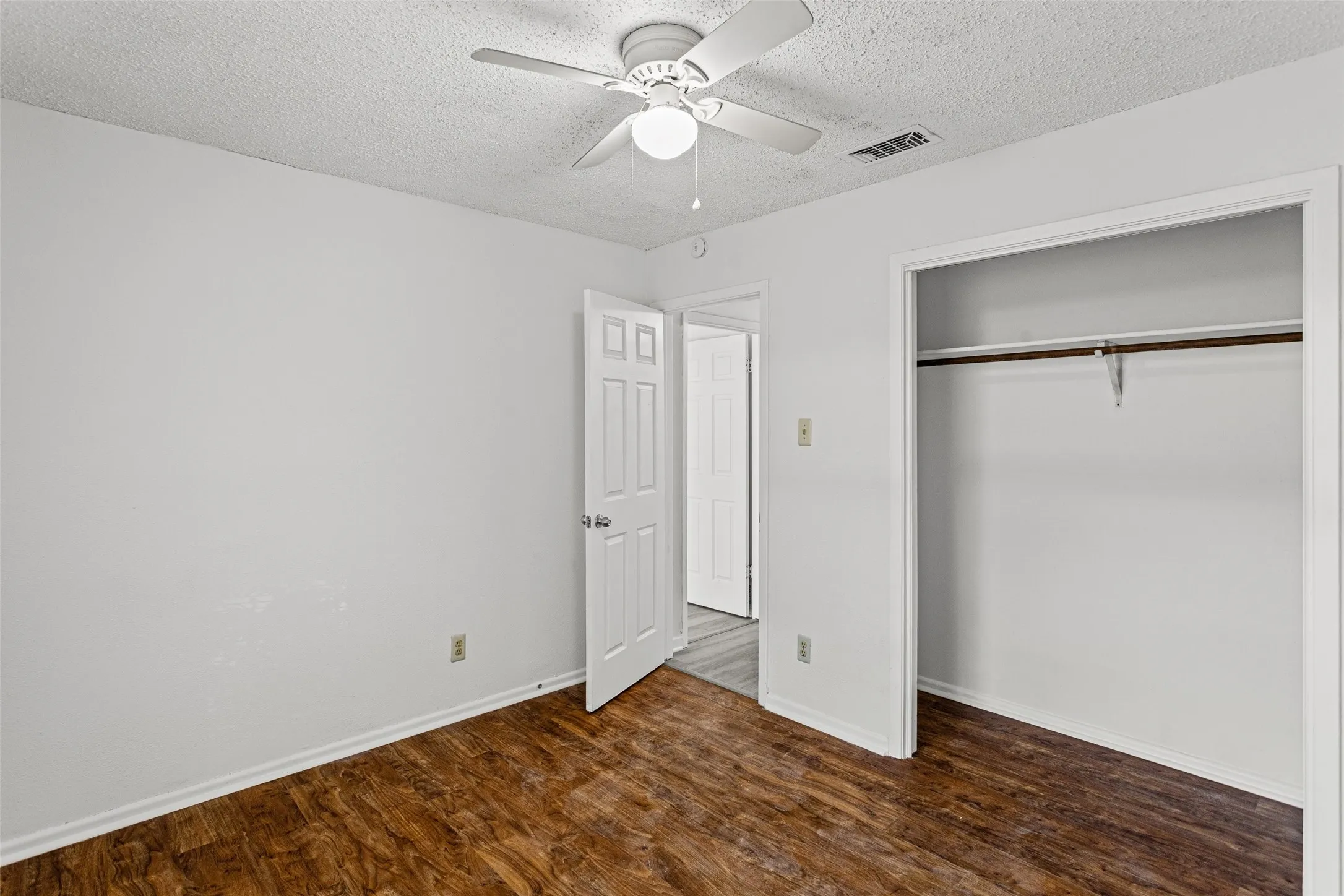 Interior room featuring wood-finish flooring, white walls, and a ceiling fan