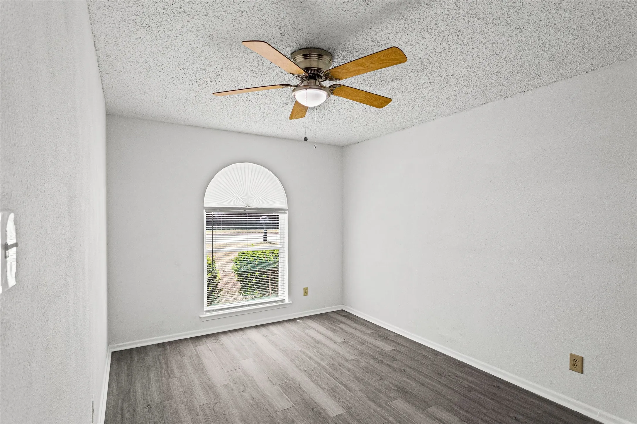 Arch-top window with pleated blind, wood-finish flooring, and ceiling fan with light fixture