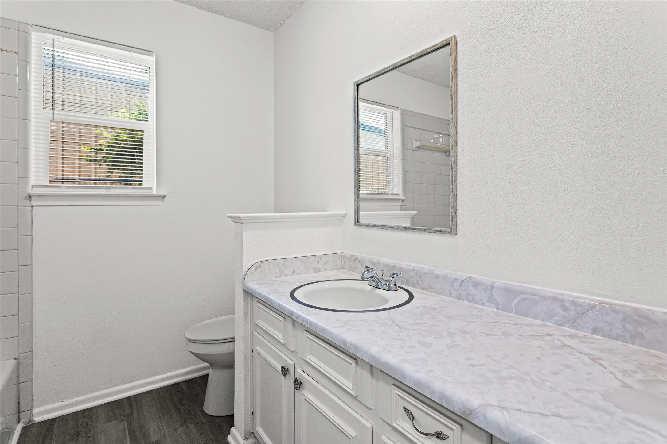 Bathroom featuring a vanity with a white countertop and integrated sink, white cabinetry with dark hardware, a framed mirror, and wood-finish flooring