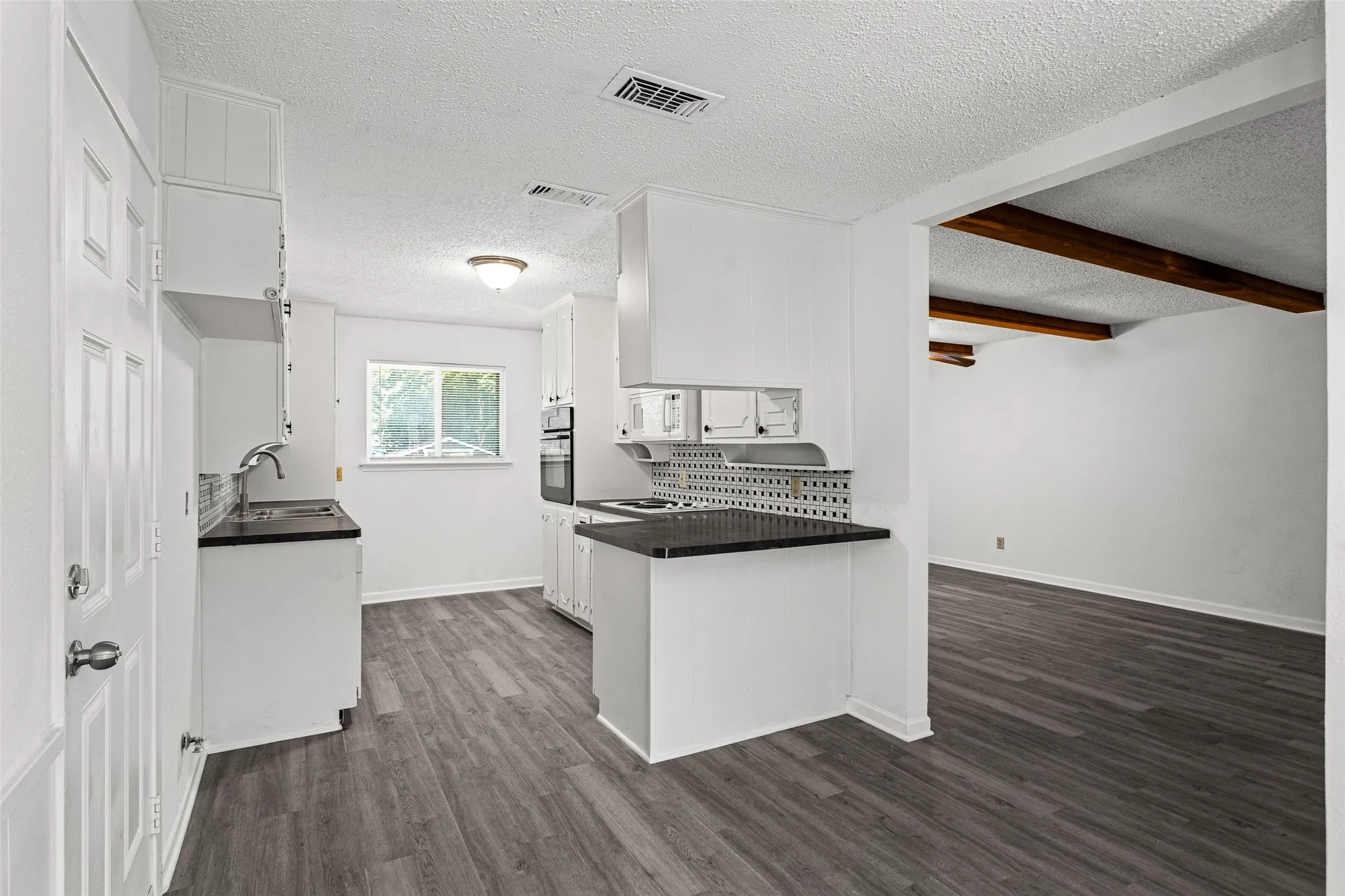 Kitchen featuring shaker-style white cabinetry, dark countertops, a tile backsplash, and wood-finish flooring
