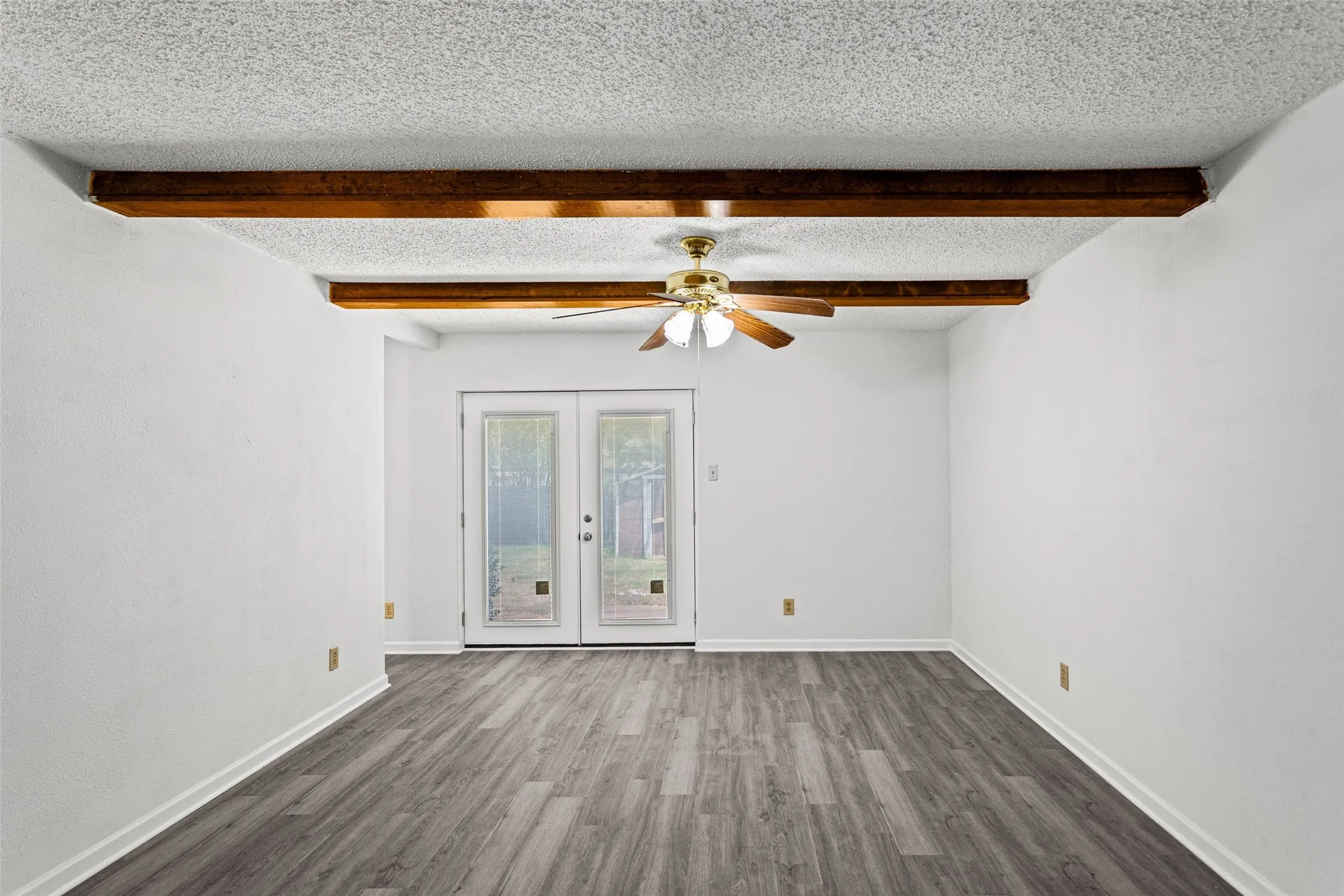 Room featuring wood-finish flooring, exposed wood ceiling beams, a ceiling fan, and double glass-paned doors