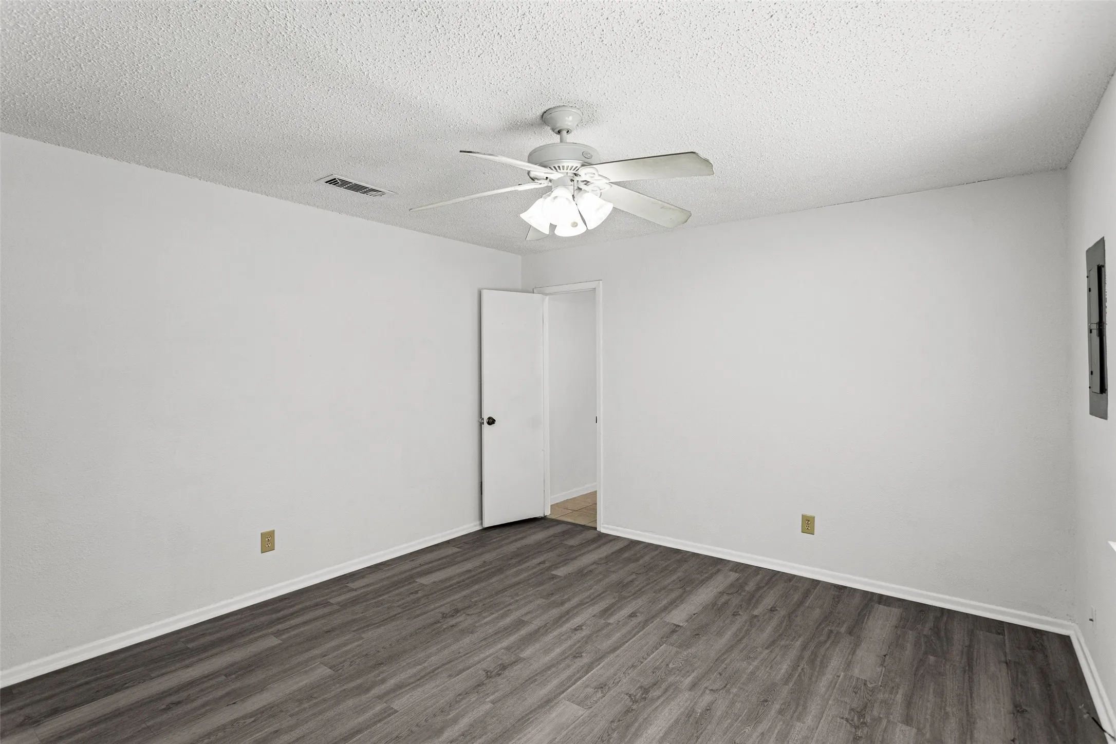 Spacious room featuring wood-finish flooring, crisp white walls, and a ceiling fan with integrated lighting
