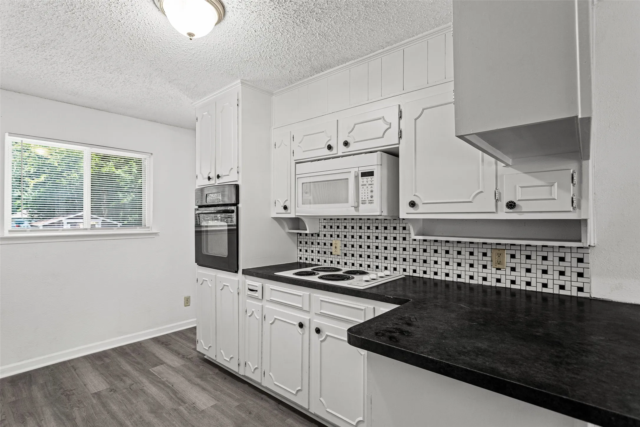 Kitchen featuring white cabinetry, black countertops, a built-in double oven, and wood-finish flooring