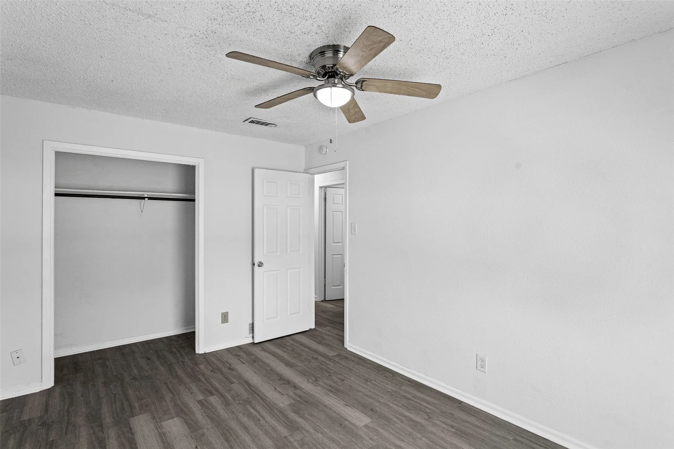 Spacious room featuring wood-finish flooring, white walls, and a ceiling fan with integrated lighting