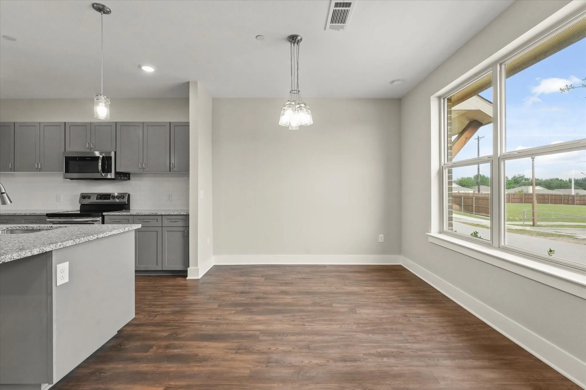 Open concept living space featuring wood-finish flooring, a kitchen island with stone-finish countertop, gray cabinetry, stainless steel appliances, and a large window with white trim