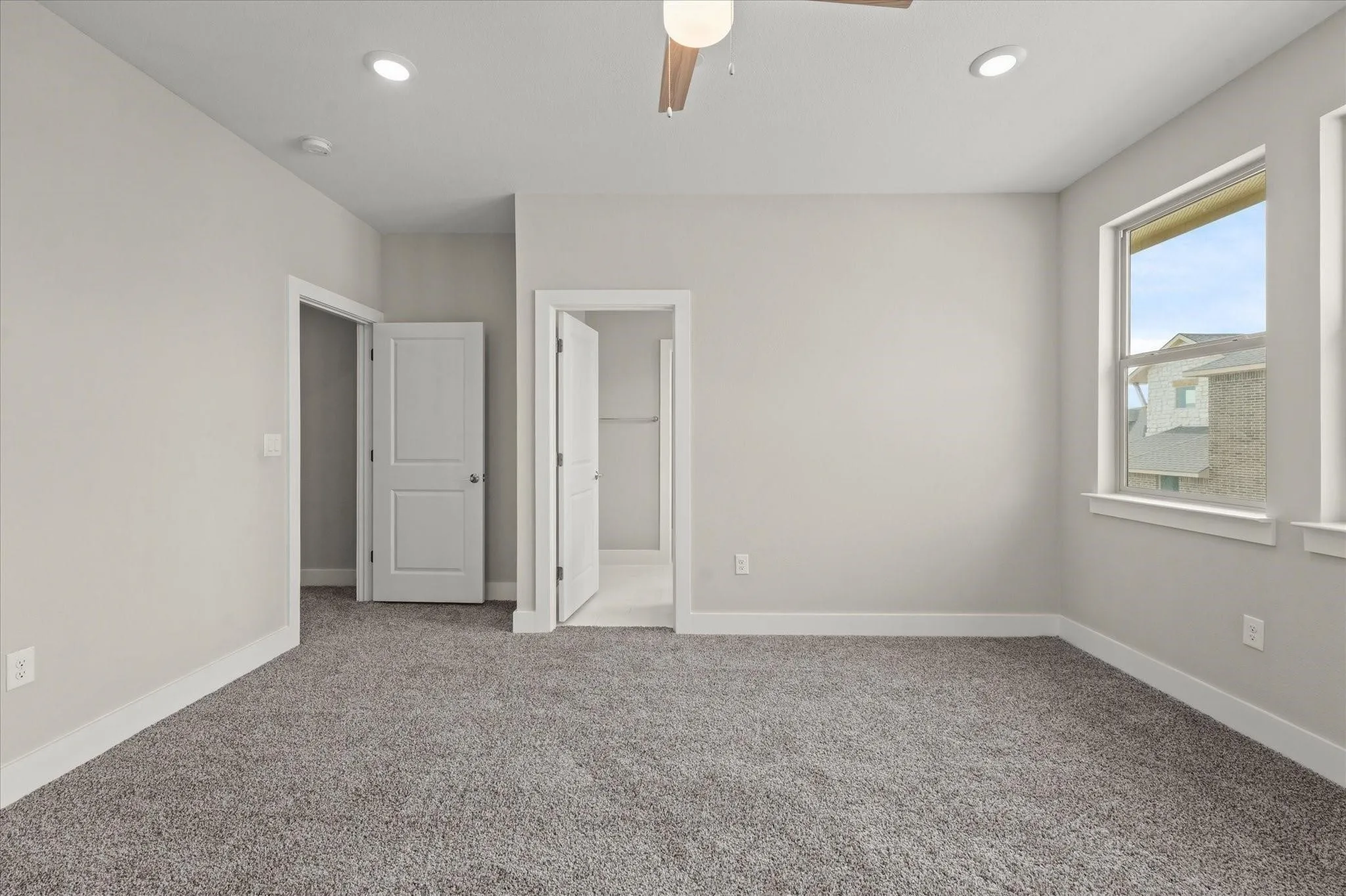 Spacious interior room featuring plush gray carpeting, neutral wall tones, two large windows, recessed lighting, and a ceiling fan