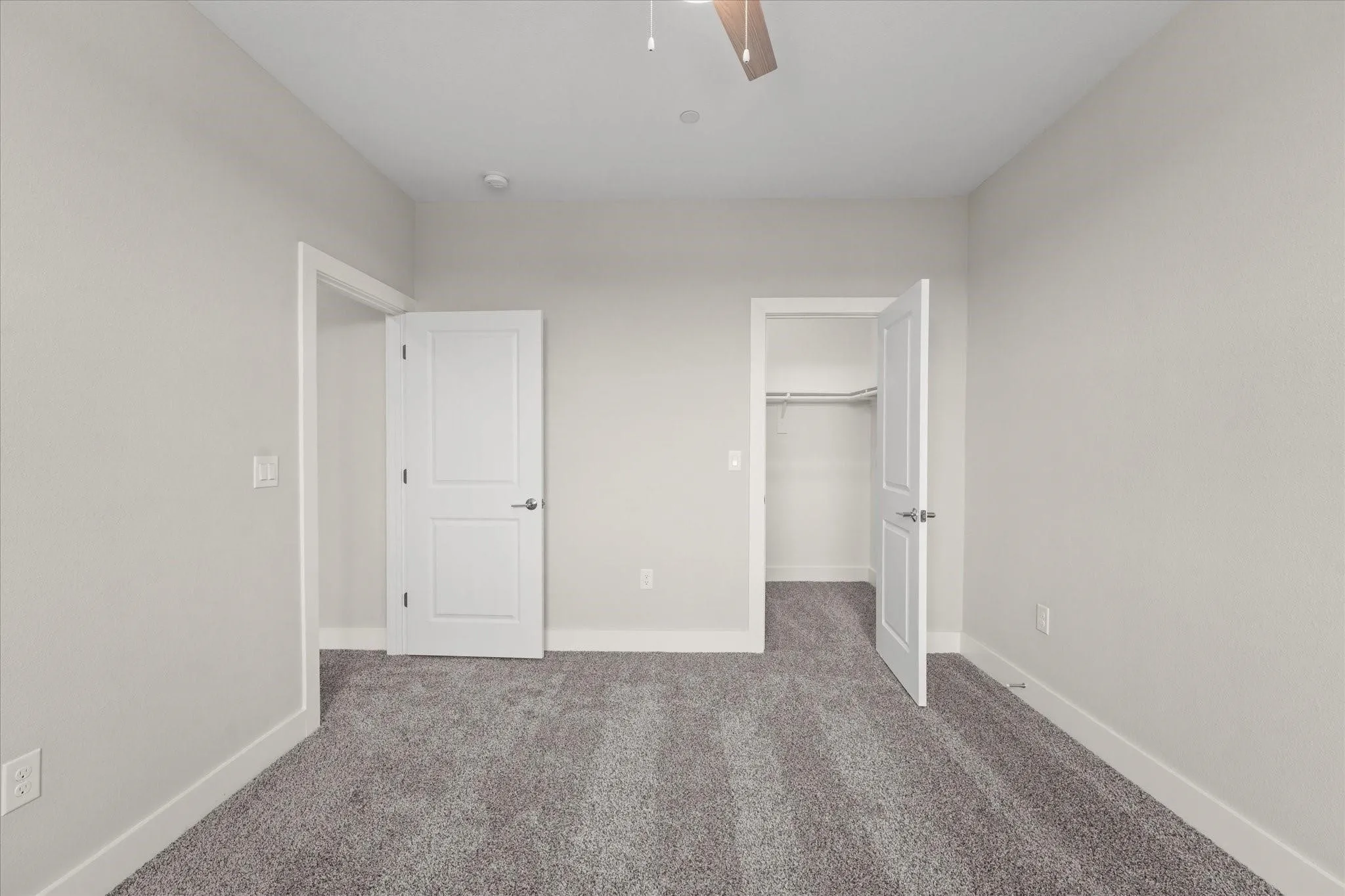 Carpeted interior room featuring light gray walls, white trim, and a ceiling fan with wood-finish blades