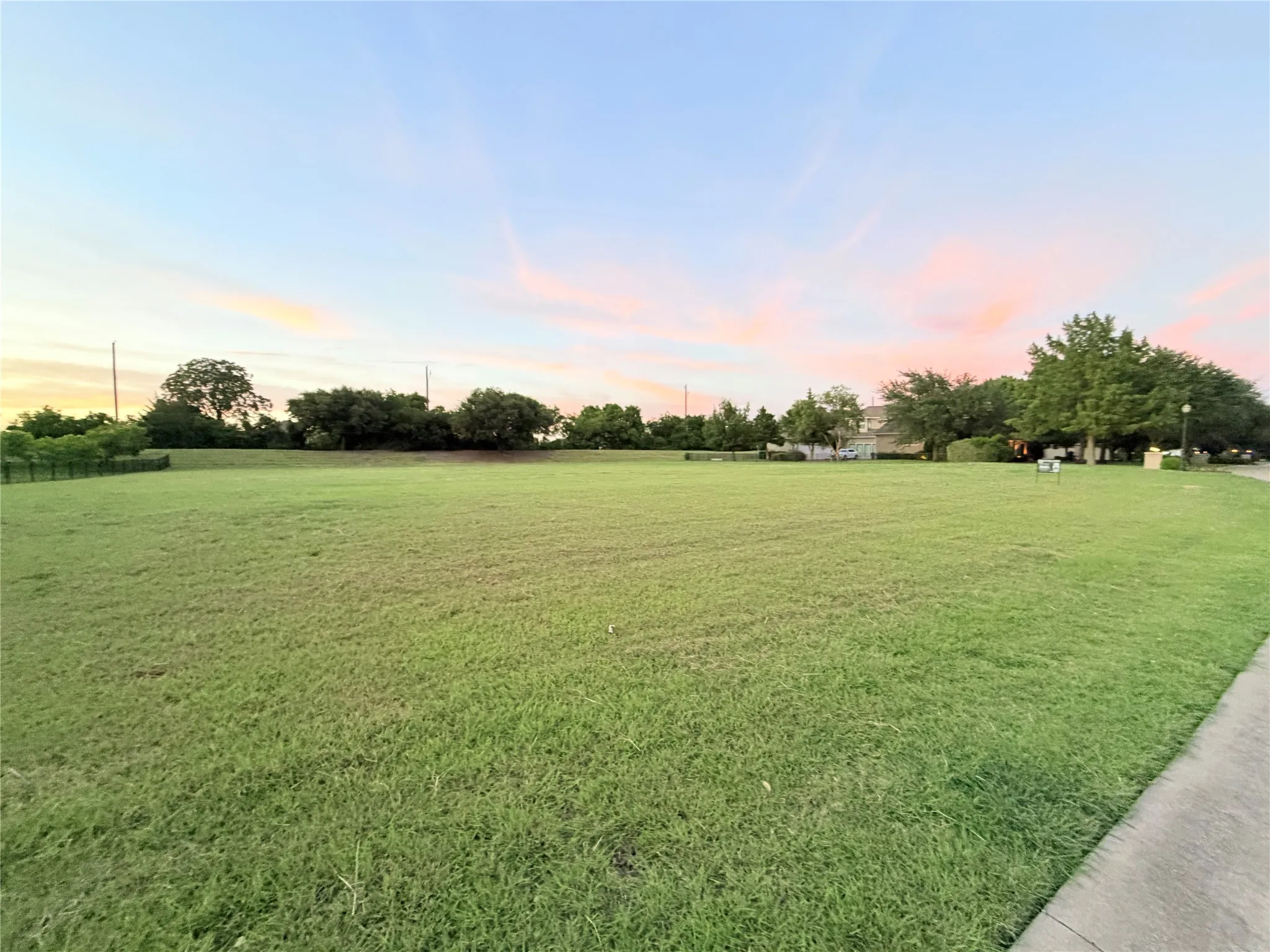 Expansive green lawn with a paved pathway, bordered by mature trees and a distant structure