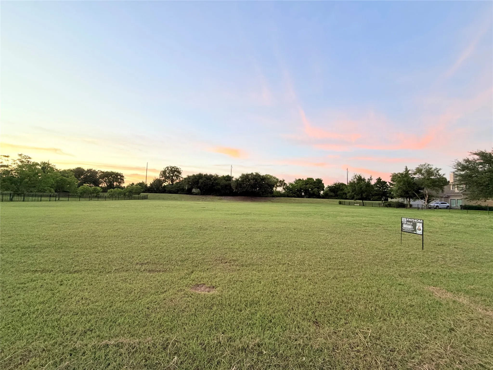 Expansive undeveloped land parcel featuring a vast grassy field and mature perimeter trees