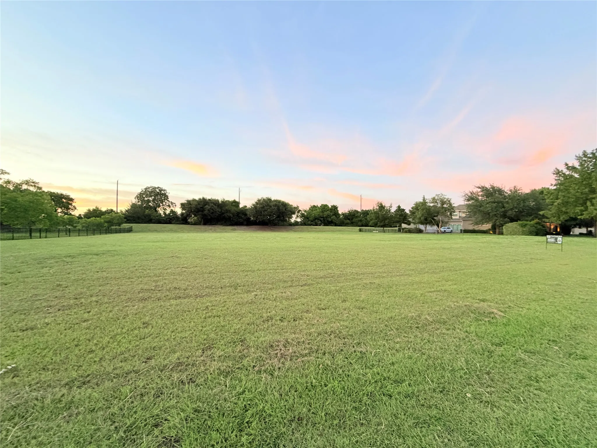 Expansive grassy lot with mature perimeter trees and a subtle horizon
