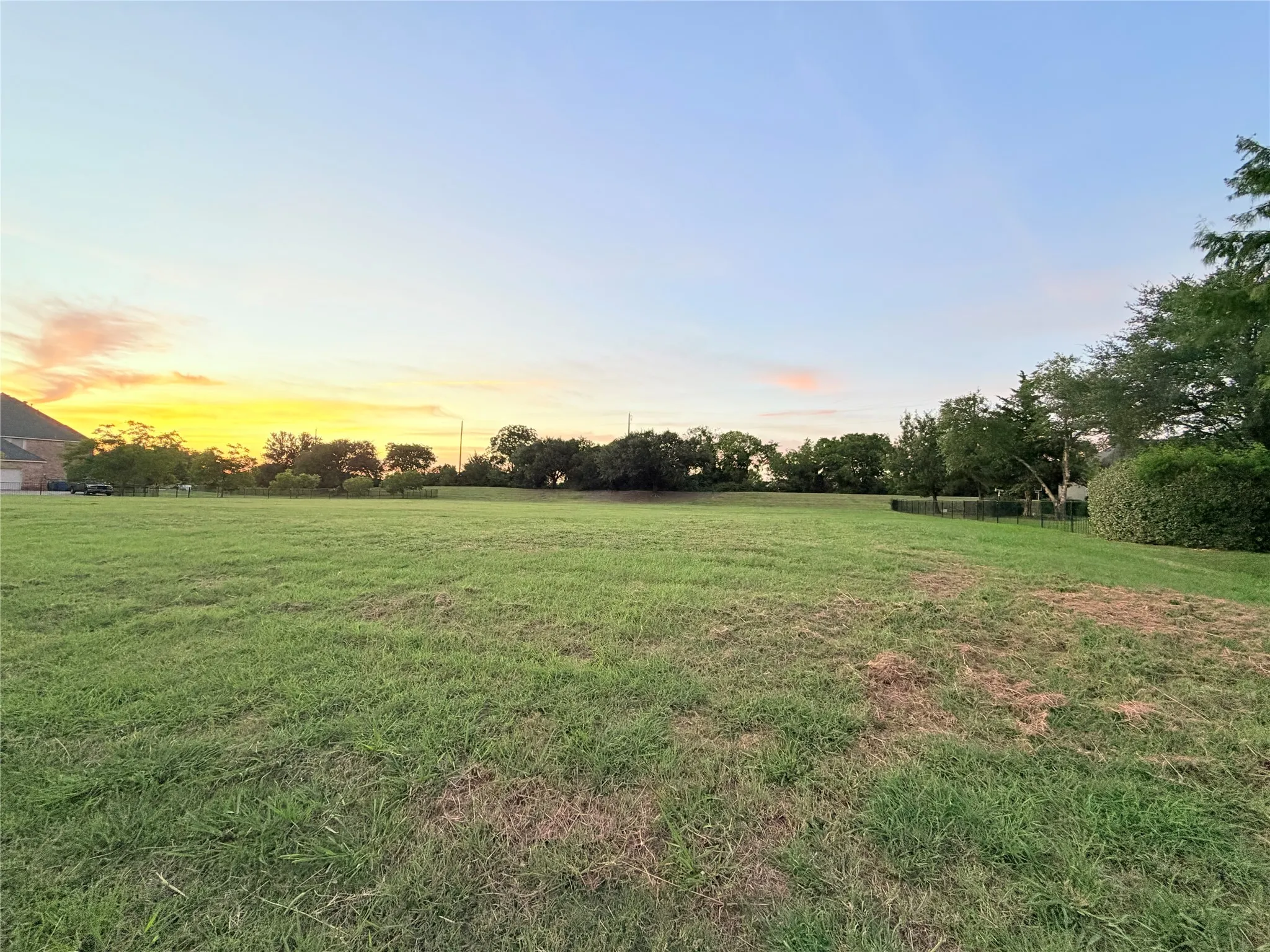Expansive green space featuring a level terrain, perimeter fencing, and mature trees in the background