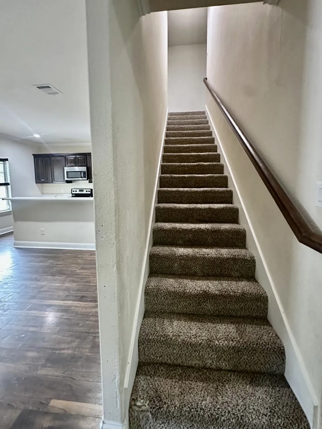 Carpeted staircase with a wood handrail, featuring white trim and walls