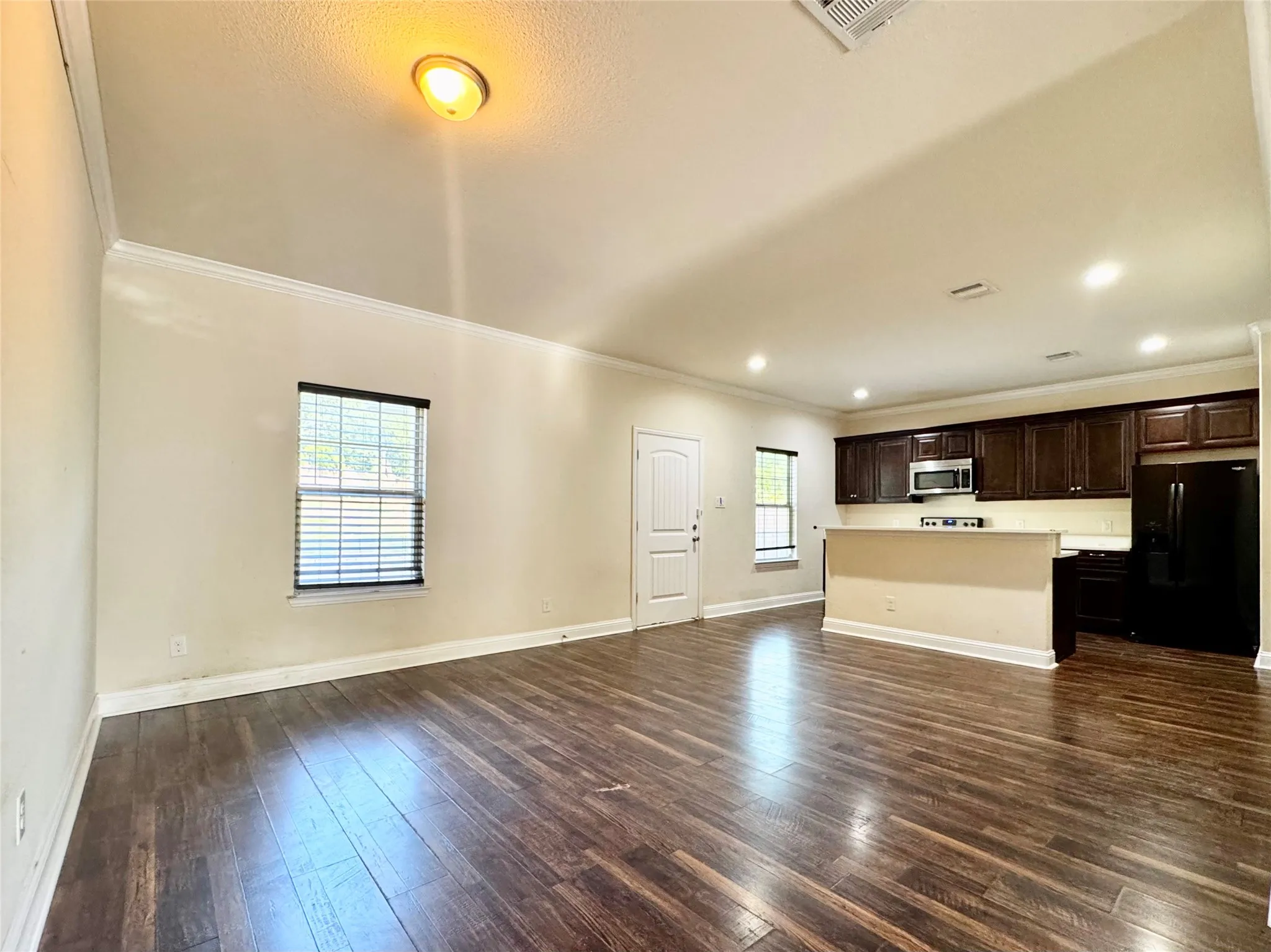 Spacious open-concept living area featuring wood-finish flooring, crown molding, and recessed lighting