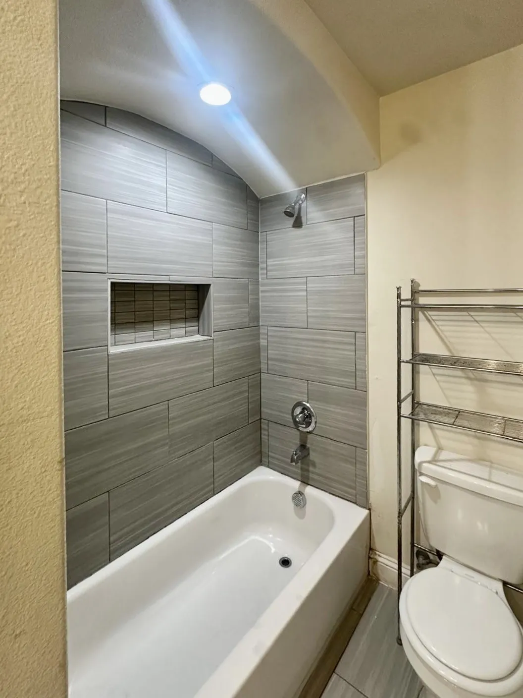 Primary Bathroom featuring a tiled shower surround with a built-in niche, white bathtub, and chrome fixtures