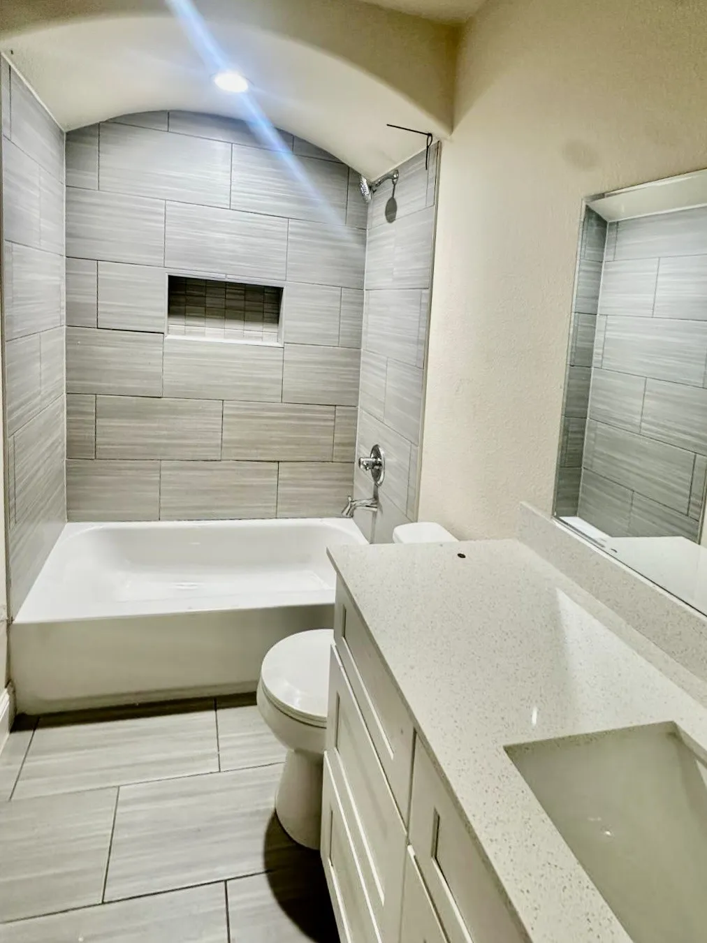 Bathroom featuring a tub/shower combination with light gray tile surround, integrated shower niche, and a white vanity with a light-colored countertop and undermount sink