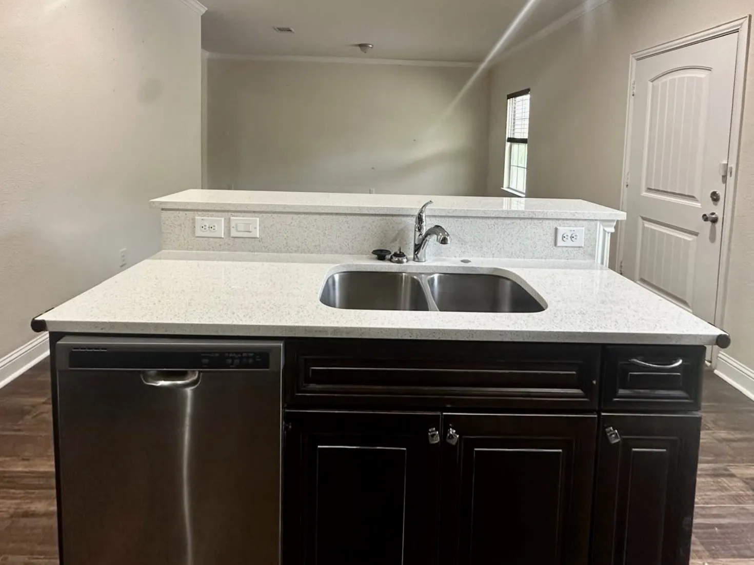 Kitchen island featuring white speckled countertops with an undermount double-basin stainless steel sink, a stainless steel dishwasher, and dark wood cabinetry