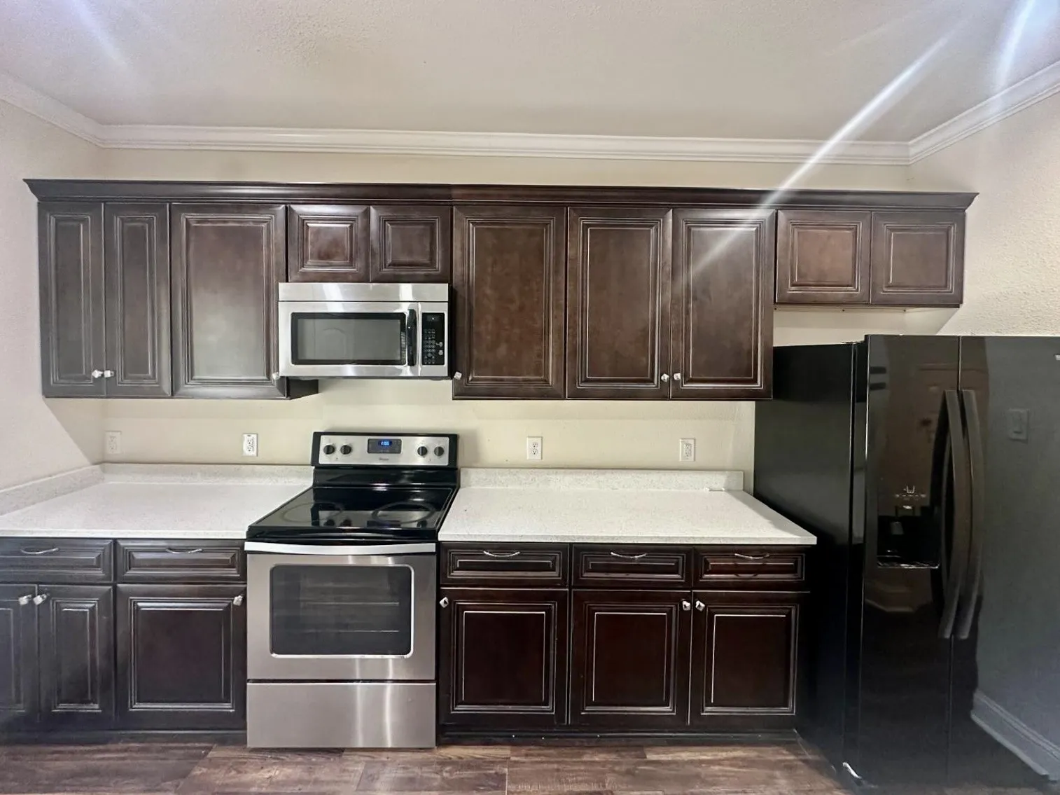 Kitchen featuring dark wood cabinetry, light countertops, stainless steel range, coordinating stainless steel microwave, and a black side-by-side refrigerator
