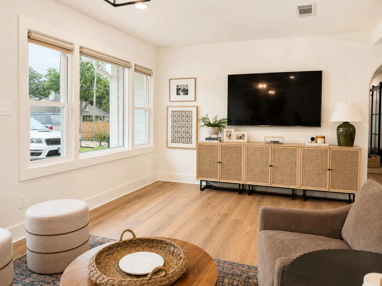 Living area featuring wood-finish flooring, white walls, and a wall of three double-hung windows with neutral blinds