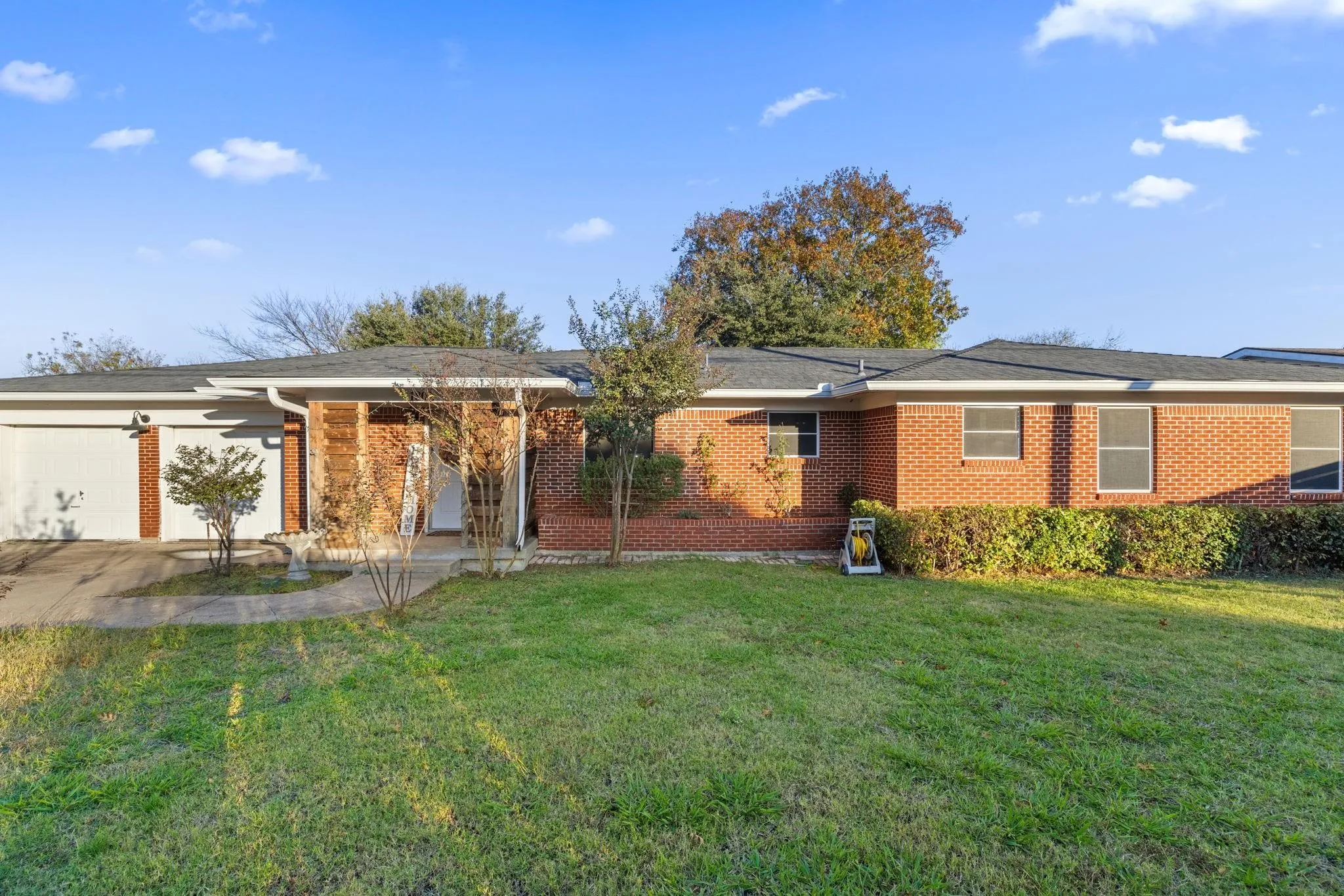 Brick exterior residence featuring a two-car garage, mature front lawn, and established perimeter shrubbery