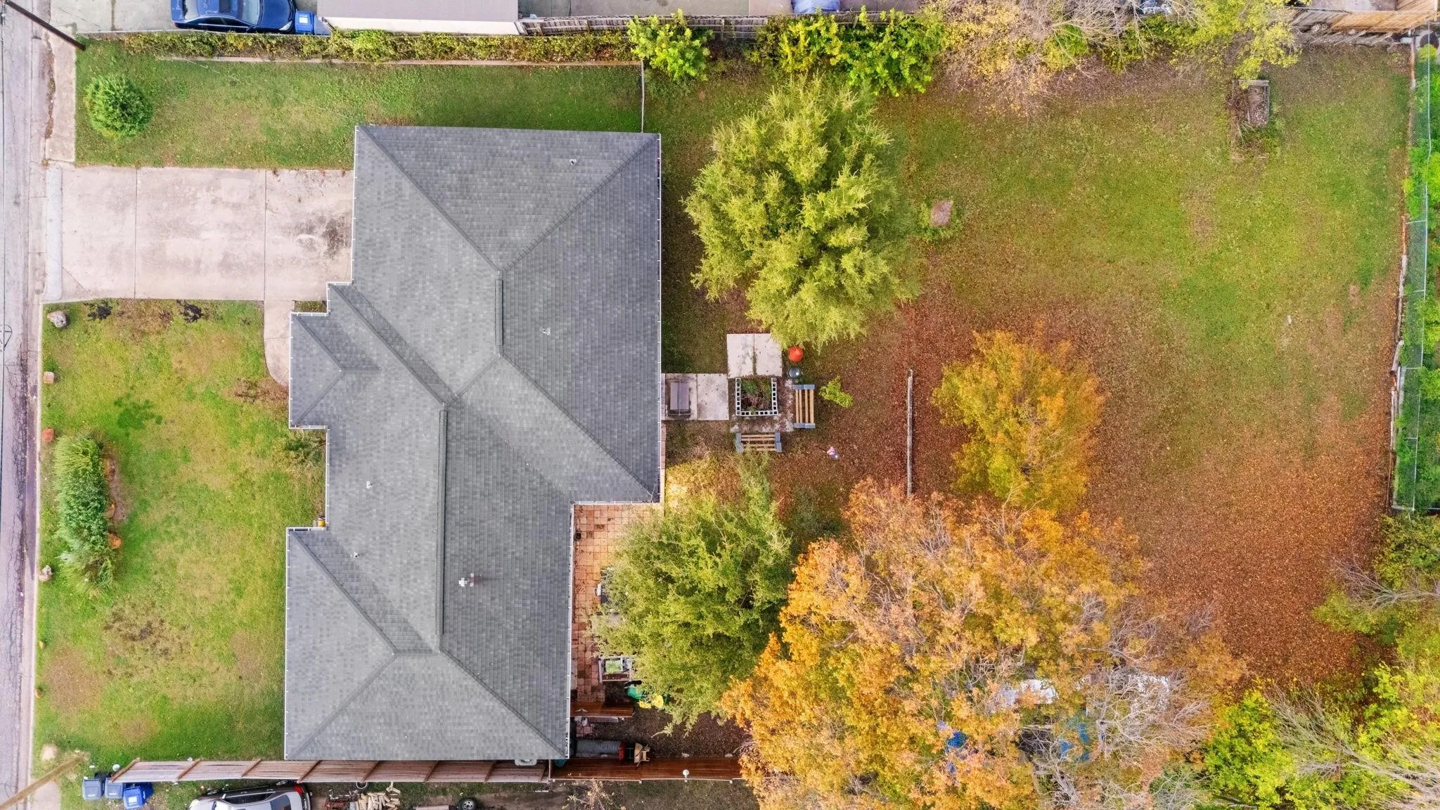 Expansive lot featuring a single-story residence with a multi-gabled roofline, a concrete driveway, and mature trees offering natural shade