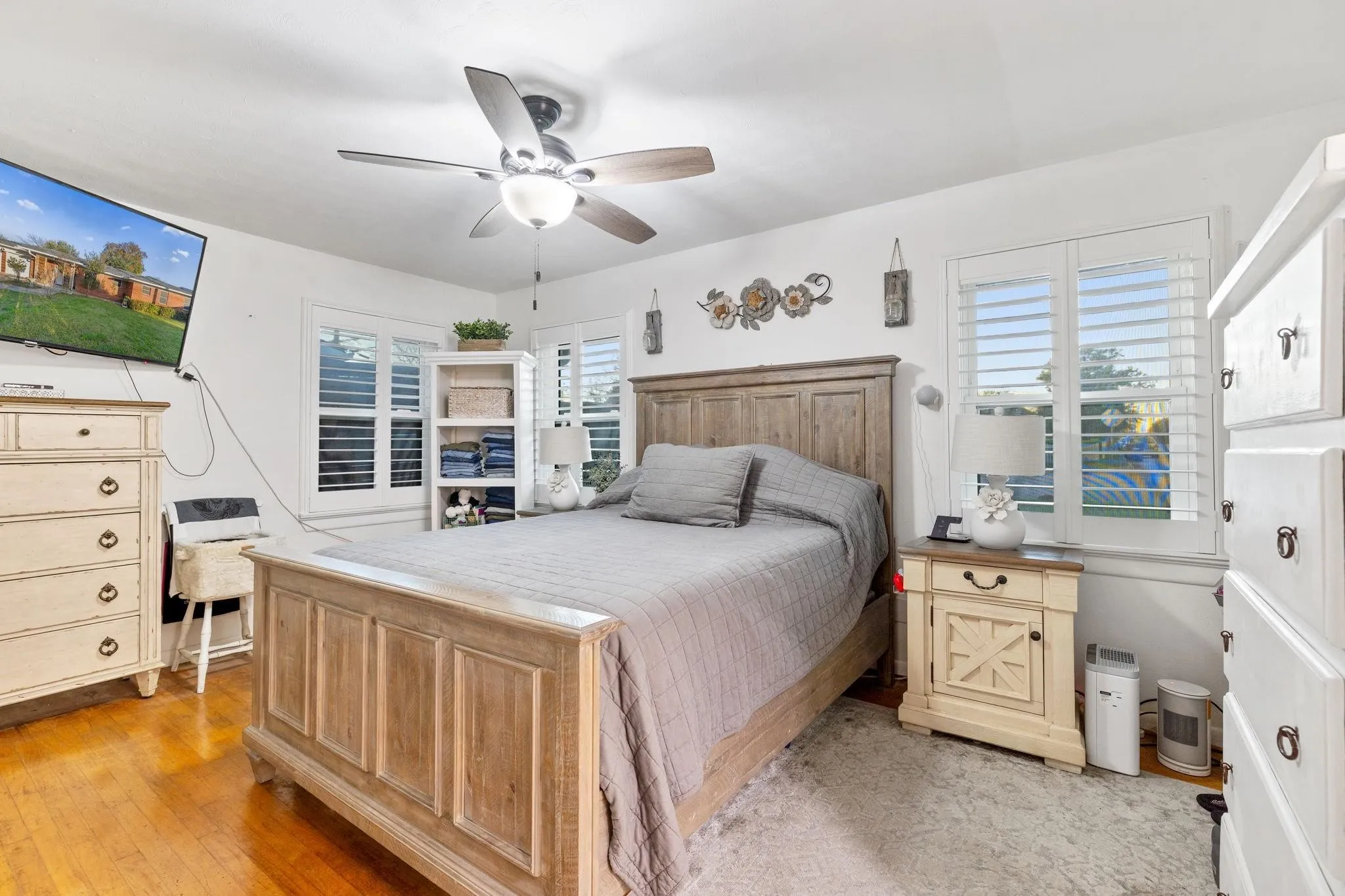 Hardwood flooring featuring a light wood bed frame, white walls, and multiple windows with white plantation shutters