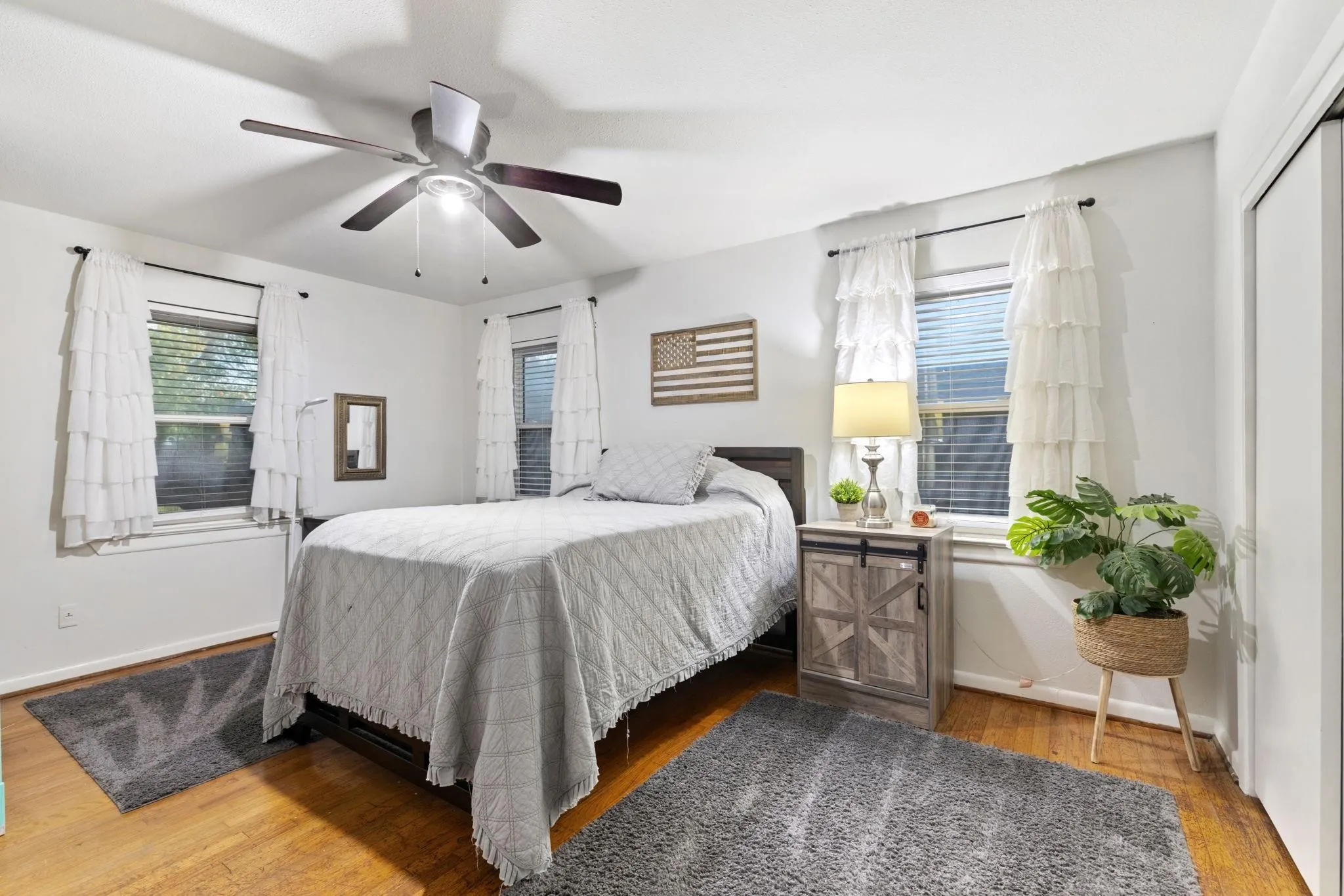 Bedroom featuring wood-finish flooring, white walls, and two windows with blinds