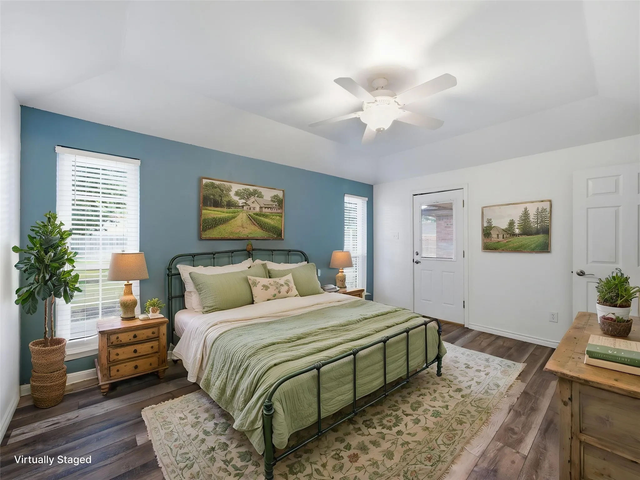 Virtually staged master bedroom featuring vaulted ceilings, wood-finish flooring, a ceiling fan, and multiple windows with blinds and a door to the backyard