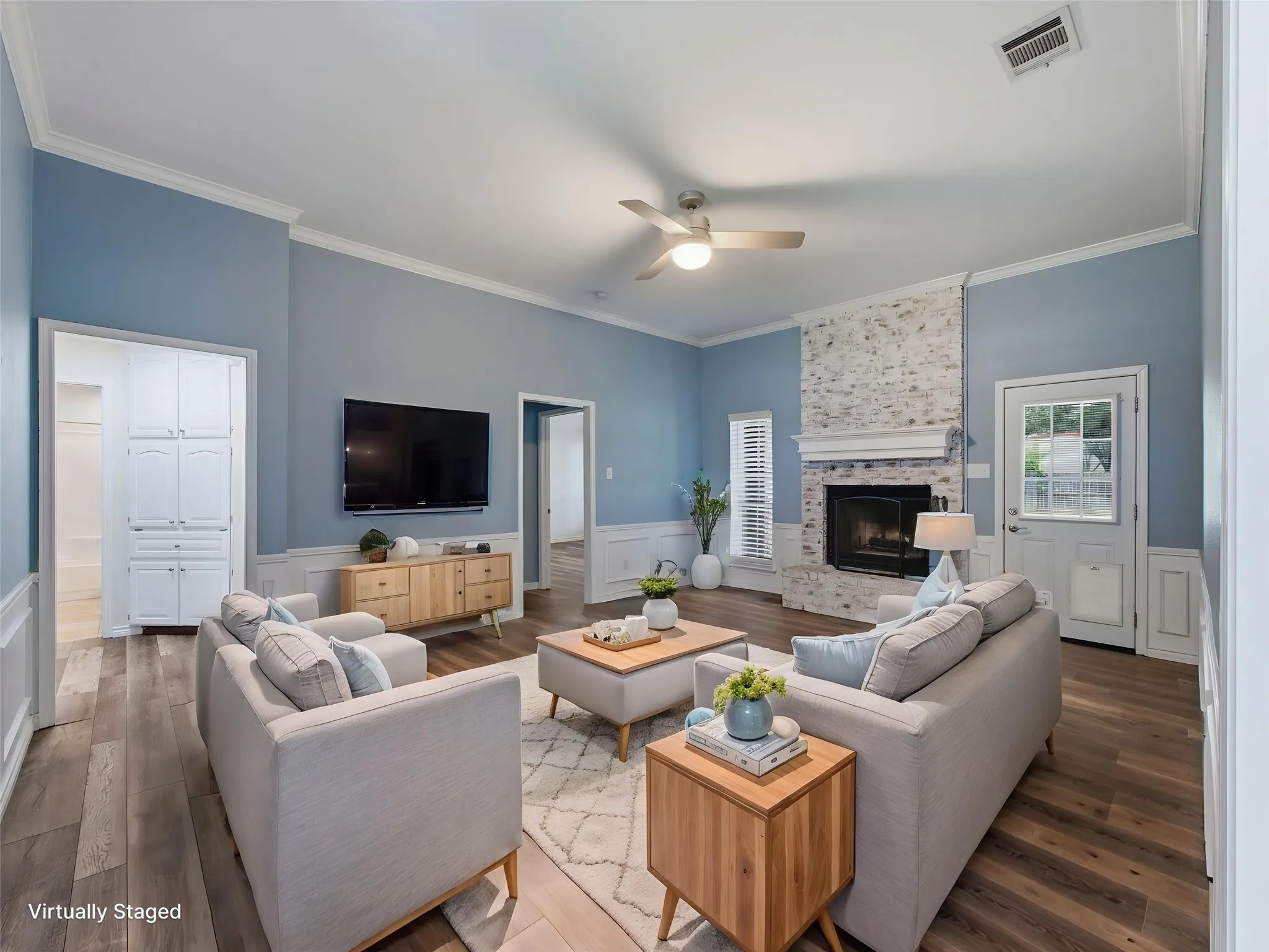 Virtually staged living area featuring wood-finish flooring, a white brick fireplace with a mantel, and crown molding