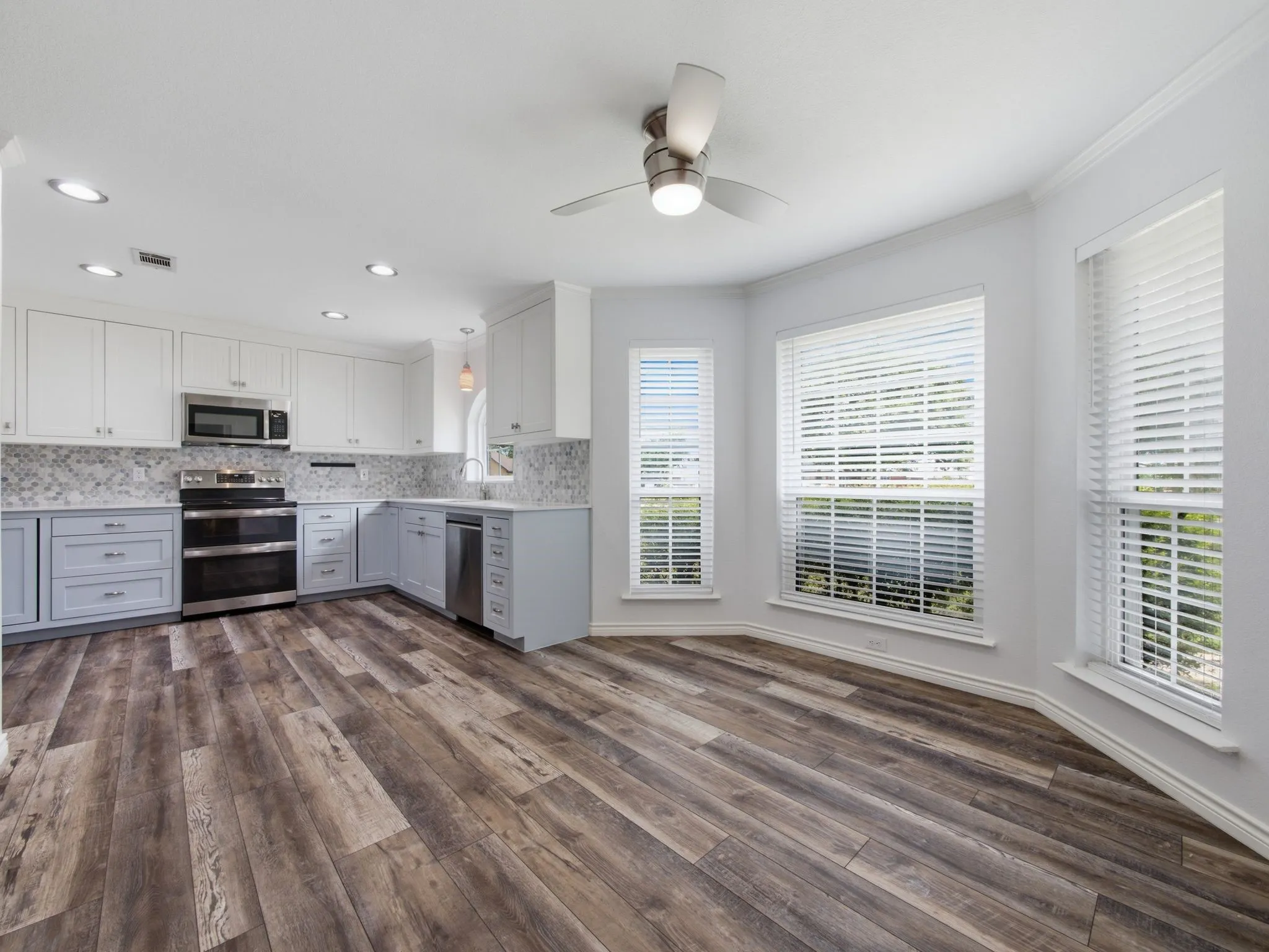 Kitchen and dining area featuring two-tone cabinetry, stainless steel appliances, wood-finish flooring, recessed lighting, and multiple windows with blinds