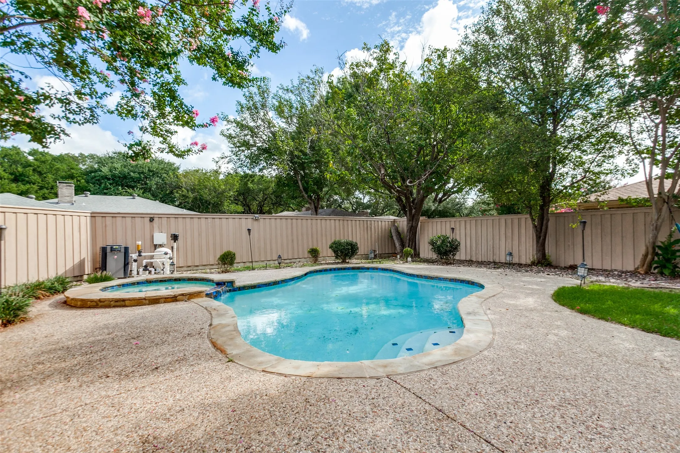 Freeform swimming pool with integrated spa and surrounding concrete patio