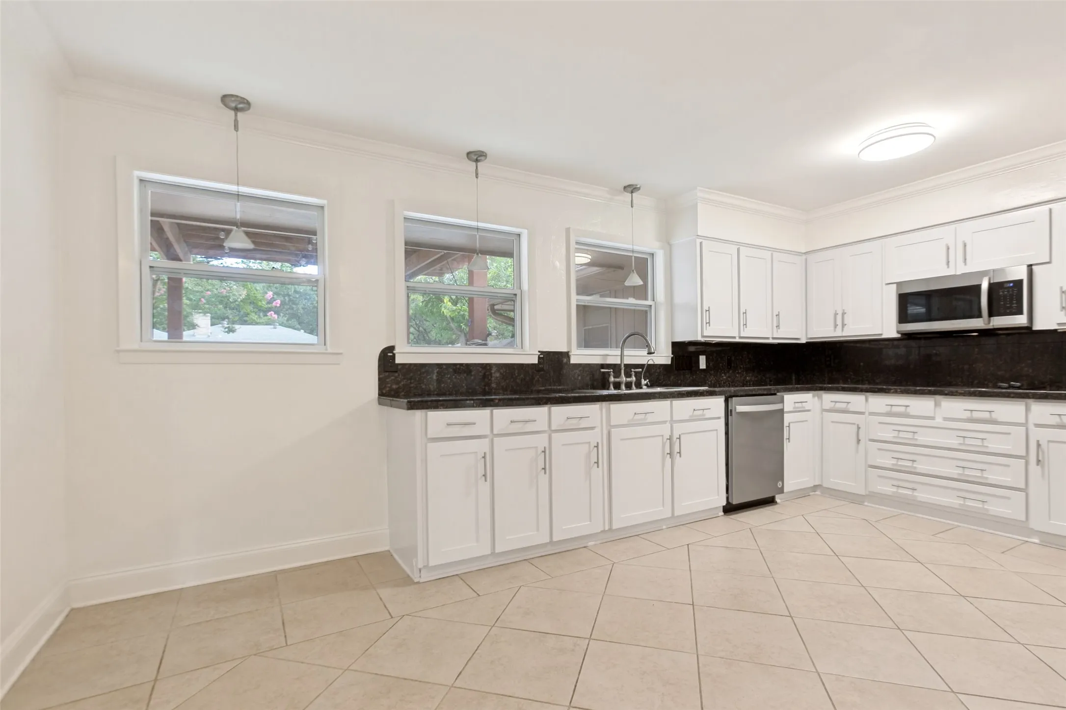 Kitchen featuring white cabinetry with brushed nickel hardware, dark countertops, stainless steel microwave, and a stainless steel dishwasher
