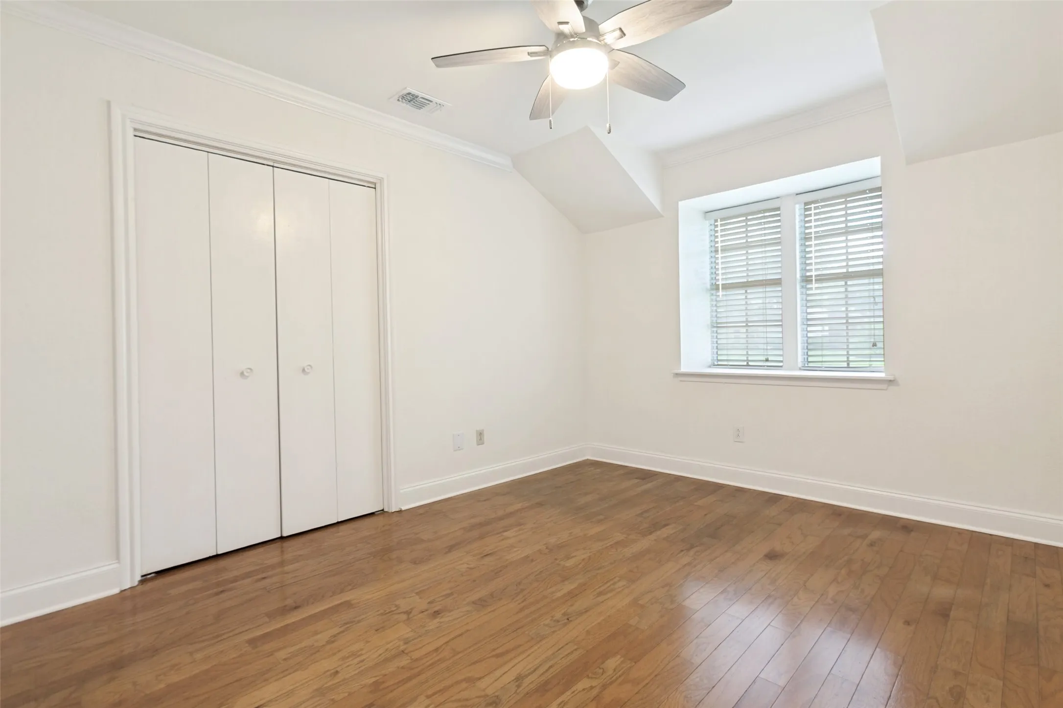Bright room featuring wood-finish flooring, a ceiling fan with integrated lighting, a window with horizontal blinds, bi-fold closet doors, and white baseboards