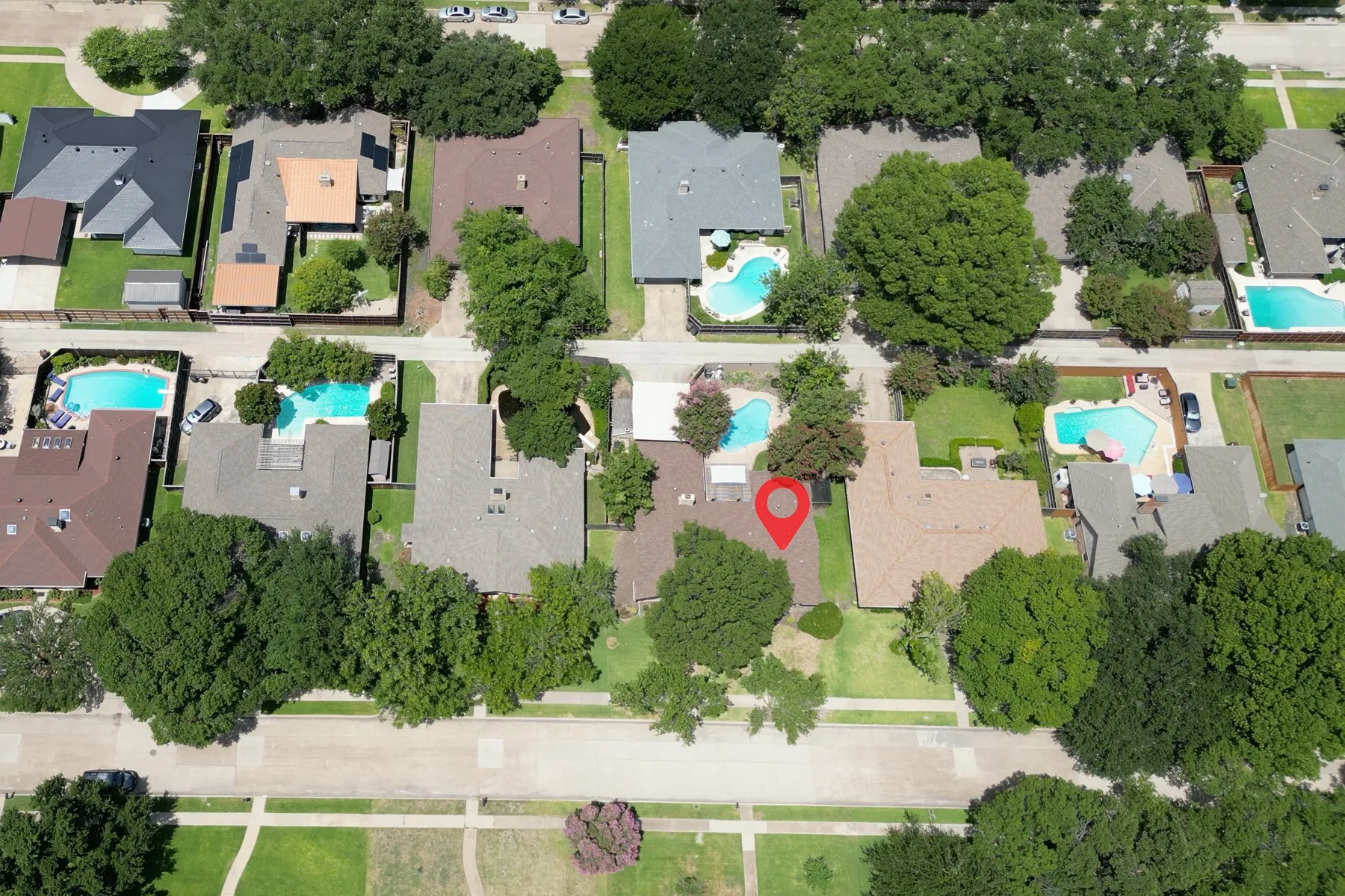 Aerial perspective highlighting the property's roofline, surrounding mature trees, and a neighborhood with multiple properties featuring private swimming pools