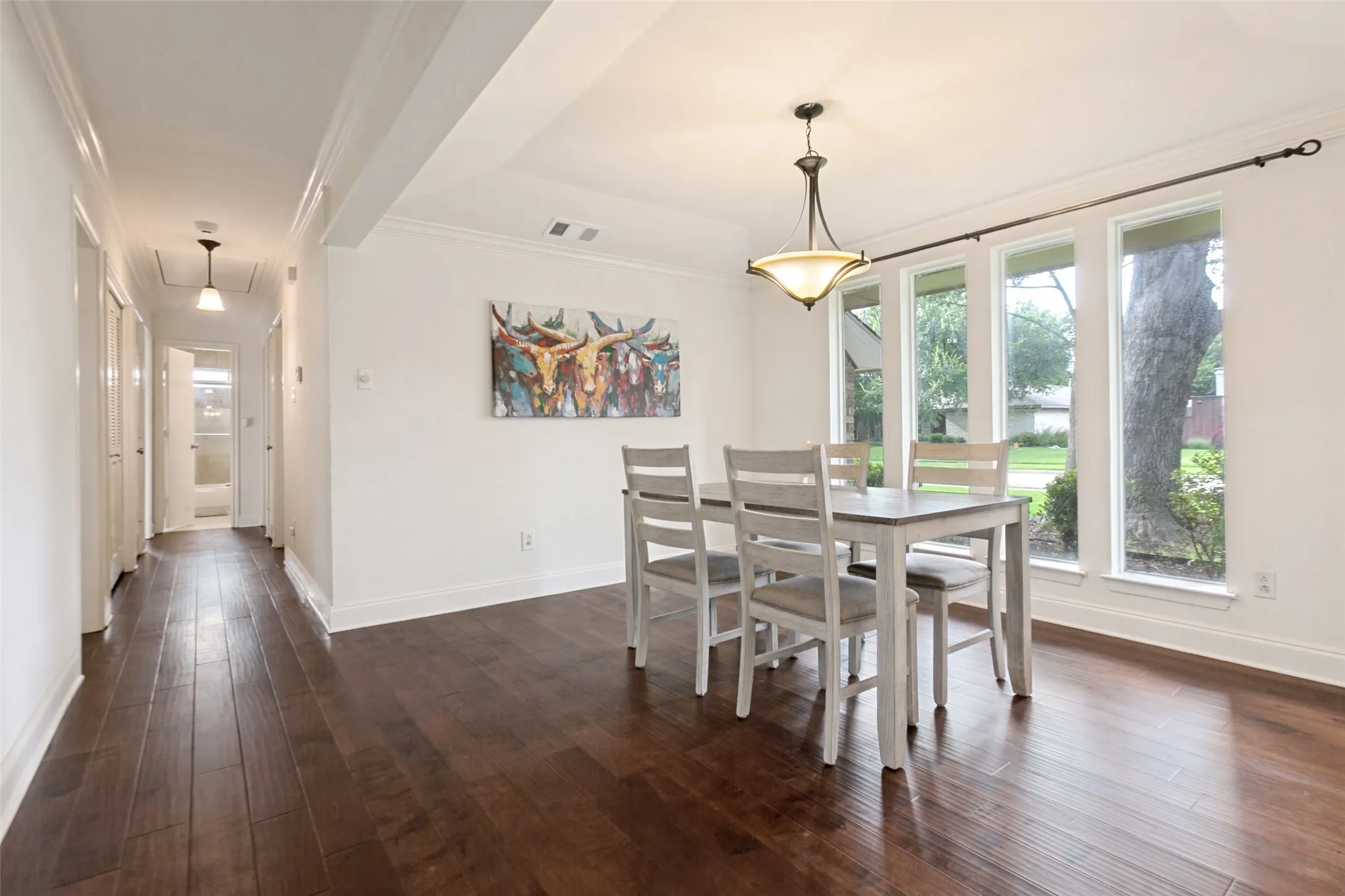Dining area with rich wood-finish flooring, white crown molding, and a series of three tall windows