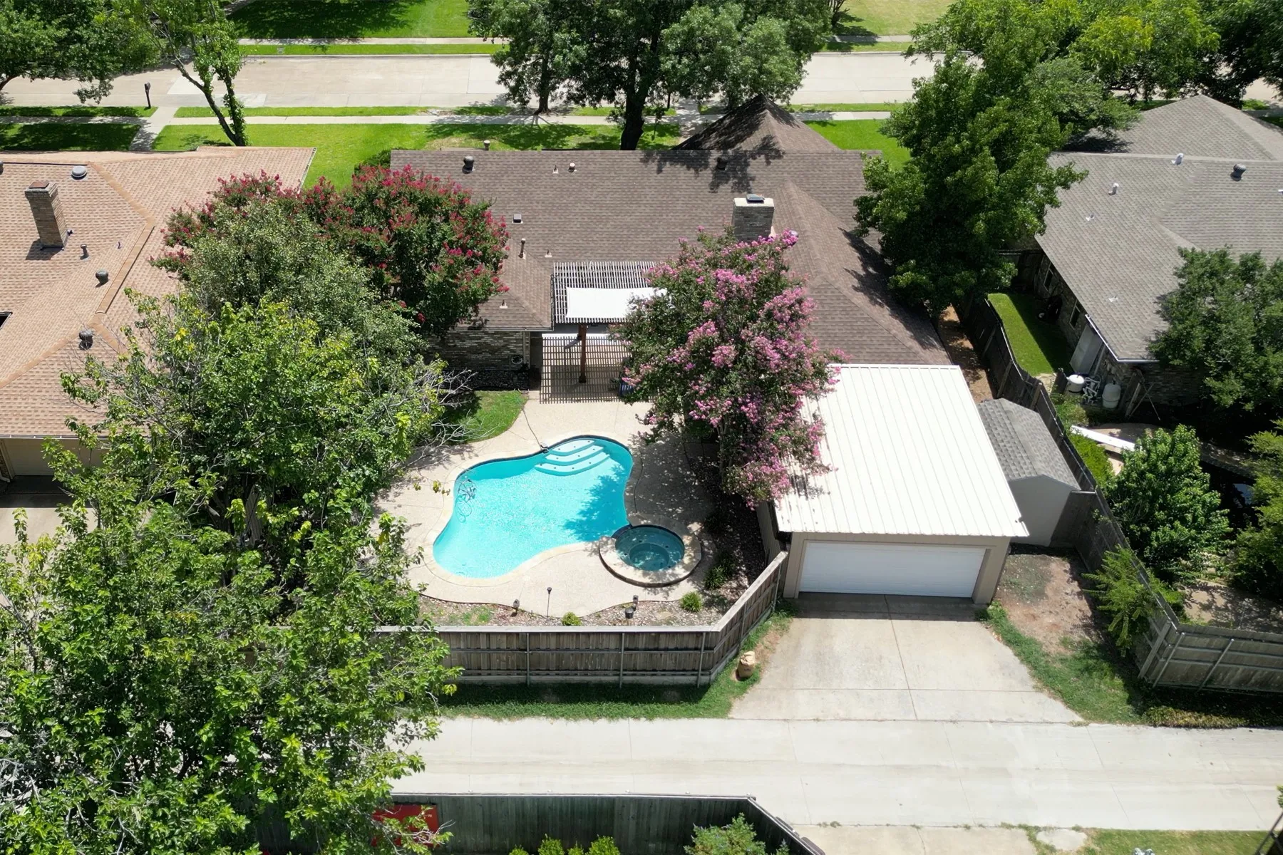 Property featuring a freeform swimming pool with integrated spa, a two-car garage with a metal roof, and mature perimeter trees