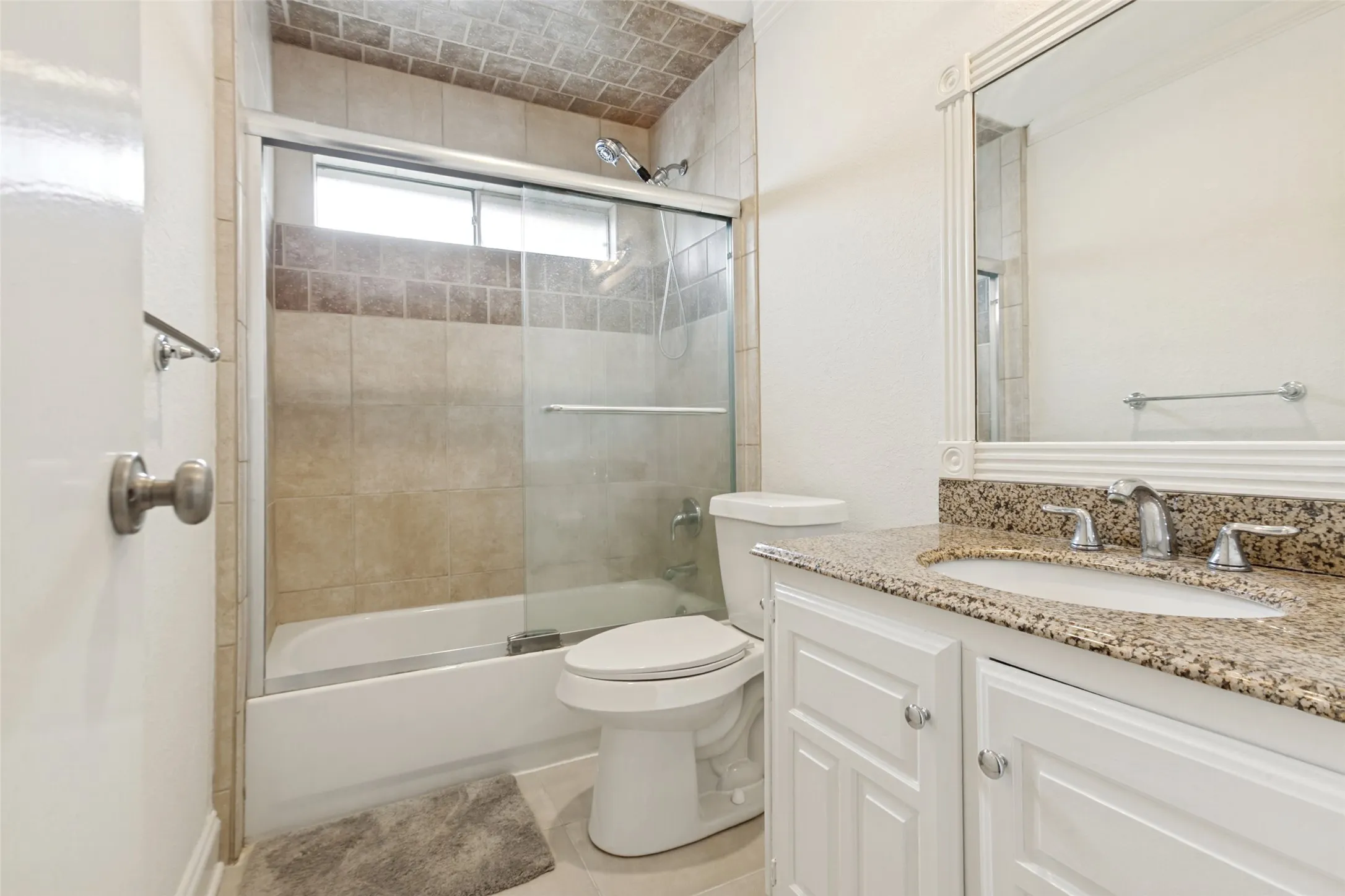 Bathroom featuring a shower-over-tub with sliding glass doors, a single vanity with stone countertop, and a framed mirror
