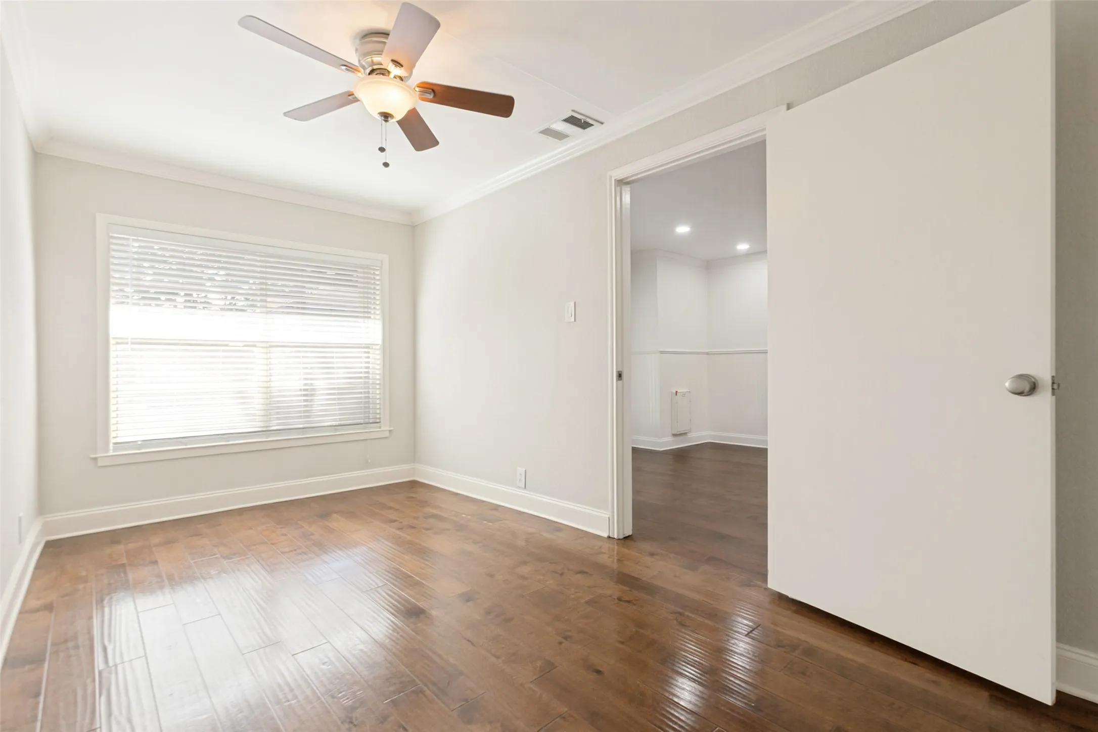 Bright room featuring wood-finish flooring, a ceiling fan with light fixture, and a large window with blinds