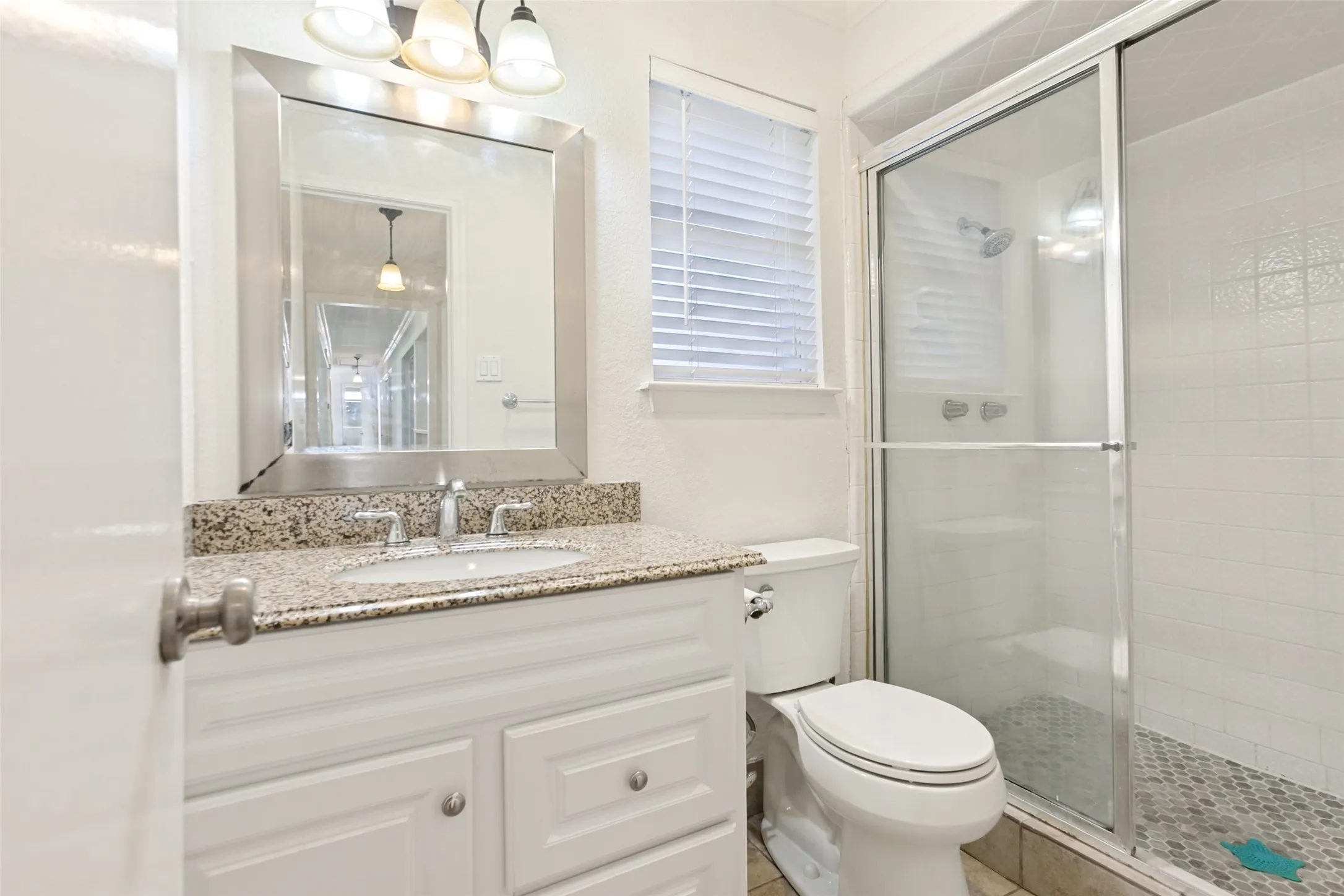 Bathroom featuring a white vanity with recessed panel doors, a speckled countertop, an undermount sink, and a framed mirror