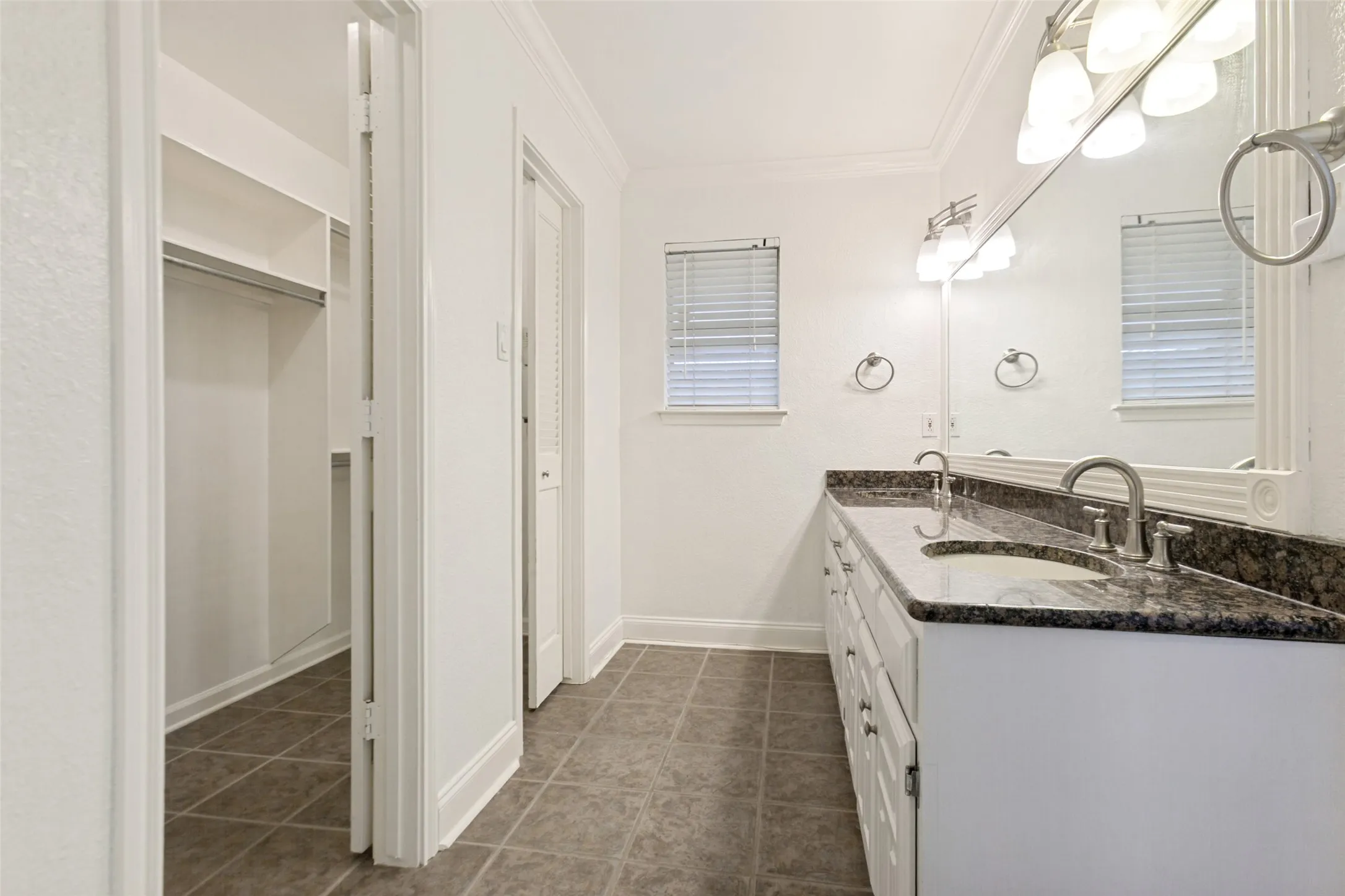 Bathroom featuring a double vanity with stone countertops and undermount sinks, flanked by two windows with blinds