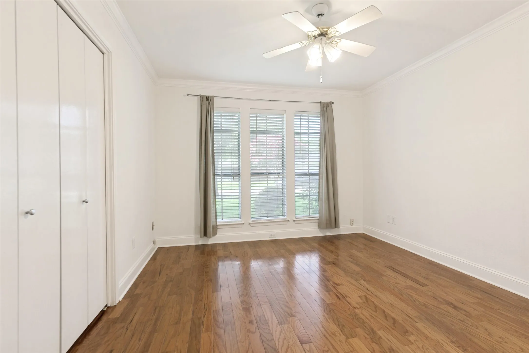 Room featuring rich wood-finish flooring, a multi-pane window with blinds, and a ceiling fan