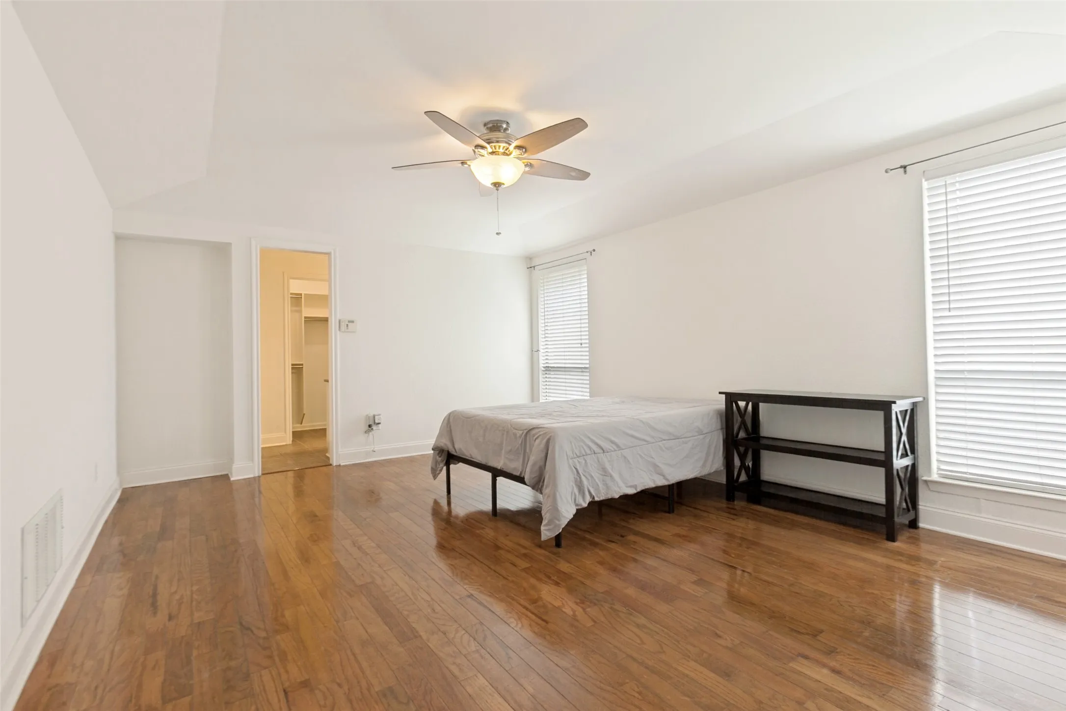 Spacious room featuring wood-finish flooring, white walls, and a ceiling fan