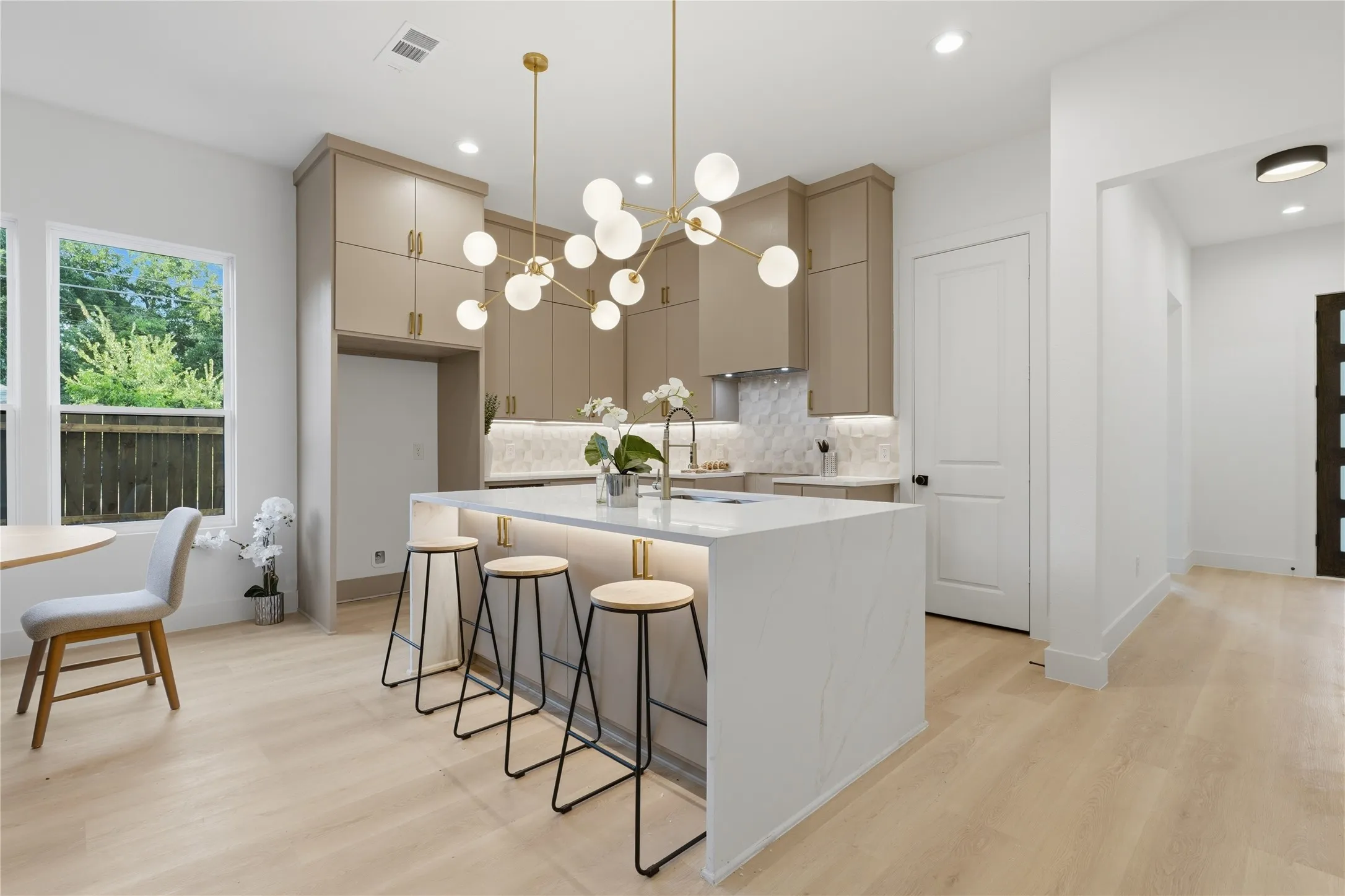 Contemporary kitchen featuring a large central island with waterfall-edge countertop, under-cabinet lighting, full-height cabinetry, a geometric tile backsplash, and light wood-finish flooring