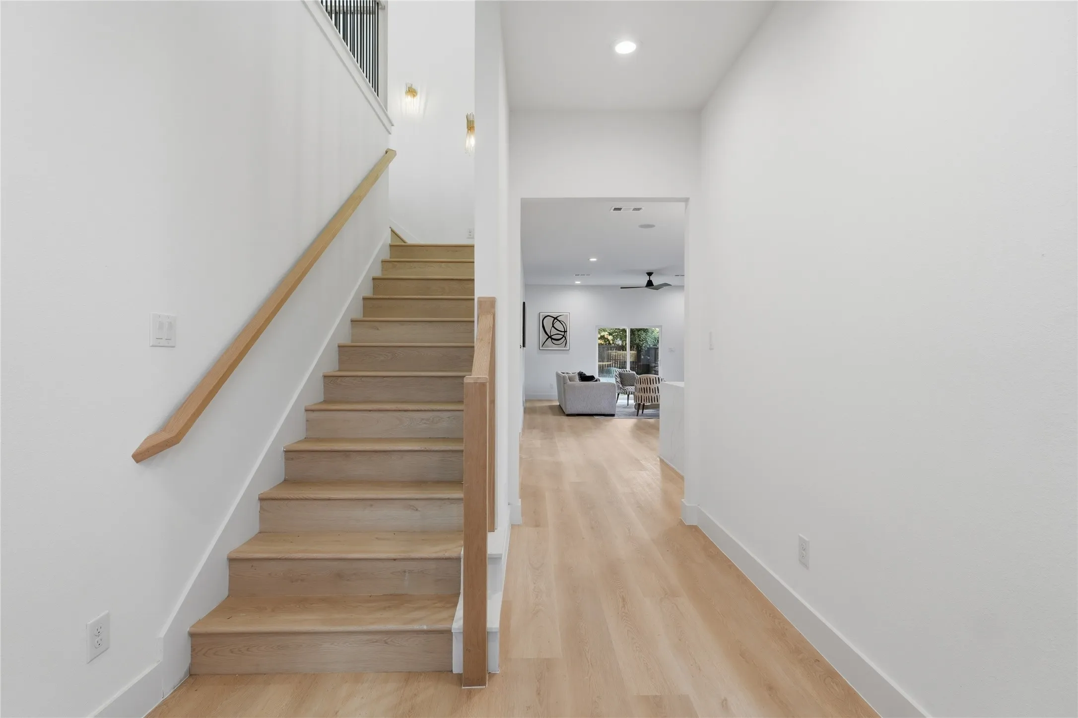 Open-tread staircase with natural wood-finish handrails and risers, complemented by white walls and recessed ceiling lighting