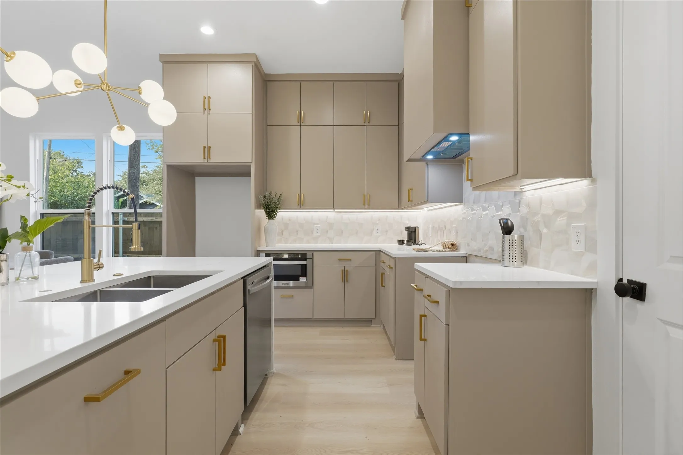 Modern kitchen featuring a large island with an undermount double sink, integrated stainless steel appliances, extensive cabinetry with brass hardware, a geometric pattern backsplash, and wood-finish flooring